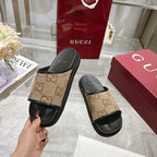 Gucci slide sandal held up: tan GG canvas strap with black rubber footbed