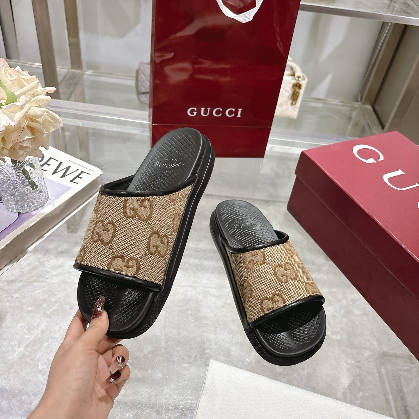 Gucci slide sandal held up: tan GG canvas strap with black rubber footbed