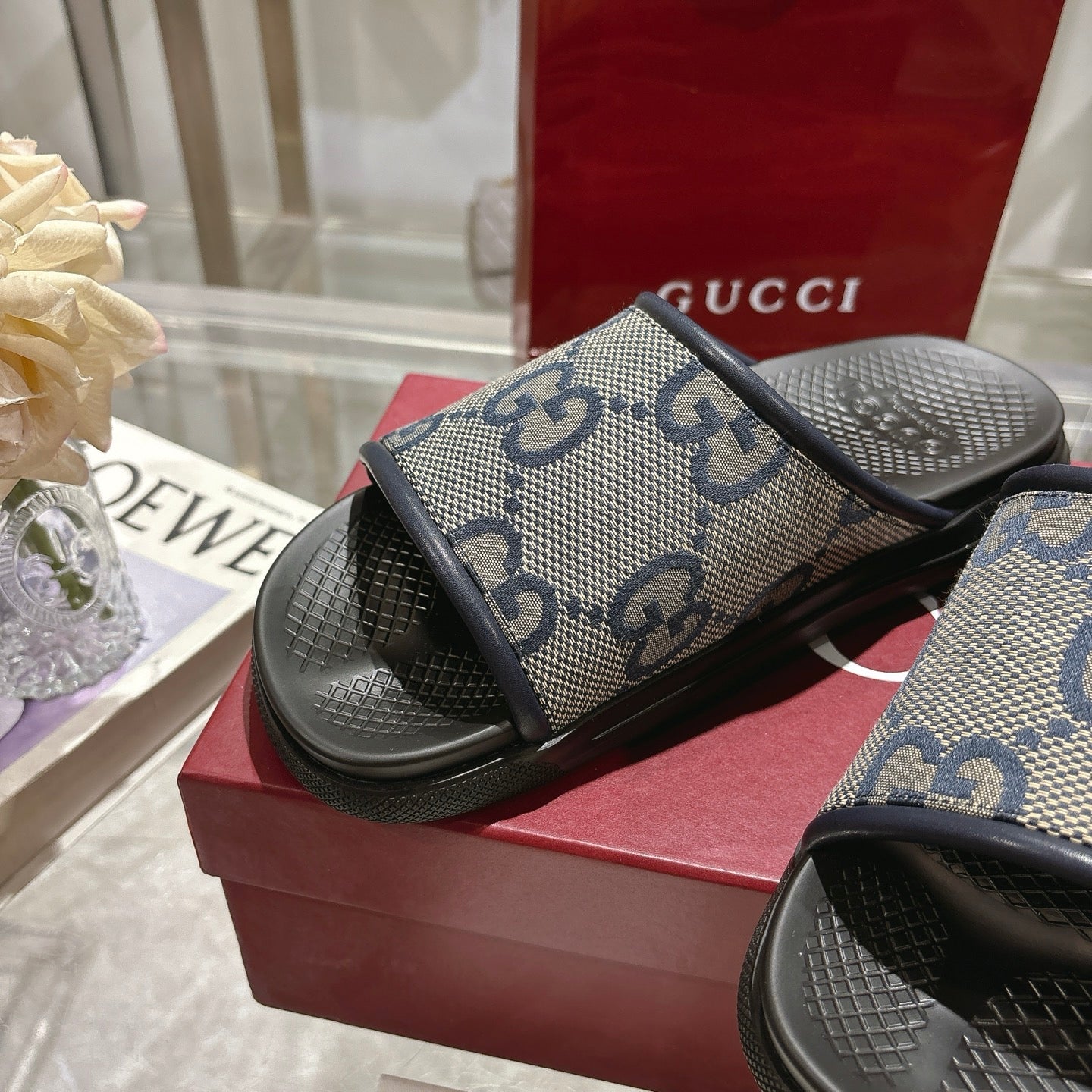Gucci slide sandals on display, GG monogram upper with black rubber footbed and strap.