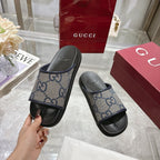 Gucci slide sandals in hand, GG monogram uppers with black rubber straps and soles.