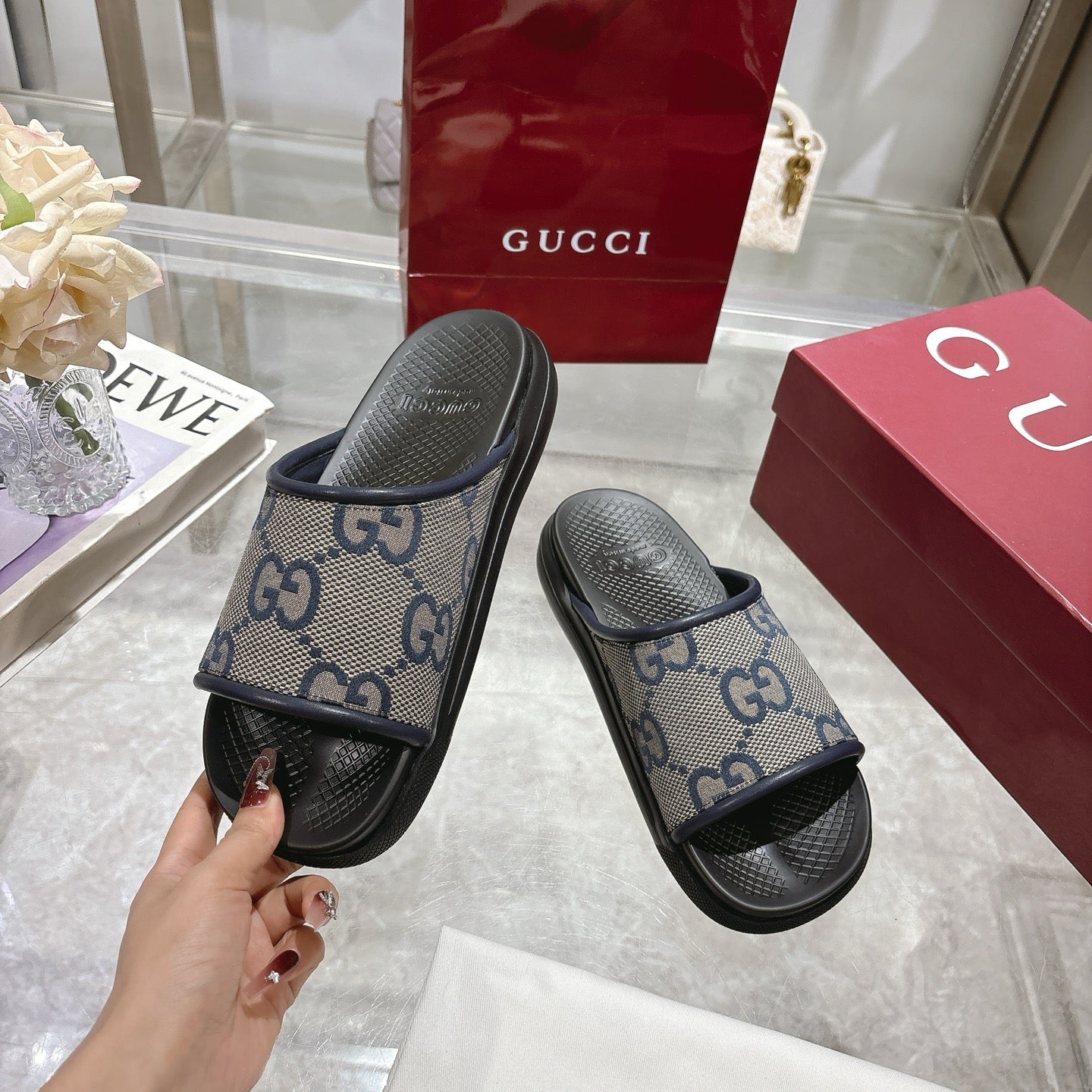 Gucci slide sandals in hand, GG monogram uppers with black rubber straps and soles.