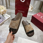 Beige GG canvas slide sandals with dark sole, lifted in hand