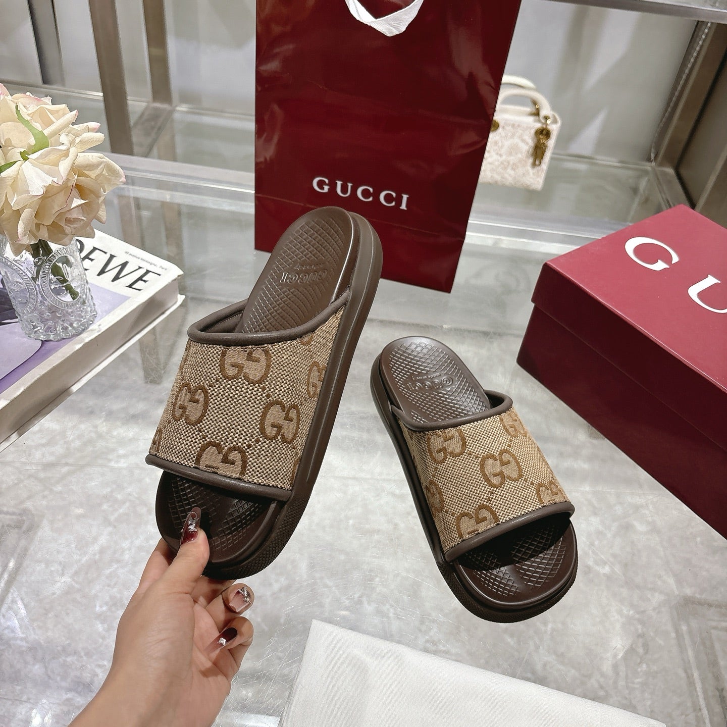 Beige GG canvas slide sandals with dark sole, lifted in hand