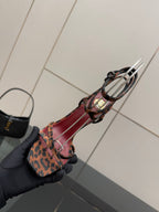Leopard print sandal with red/pink straps and black harness, gold heel accent