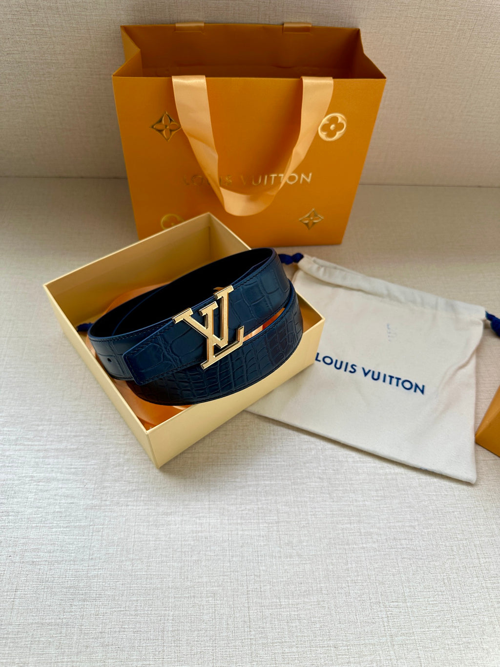 Blue embossed leather belt with LV buckle laid in open box