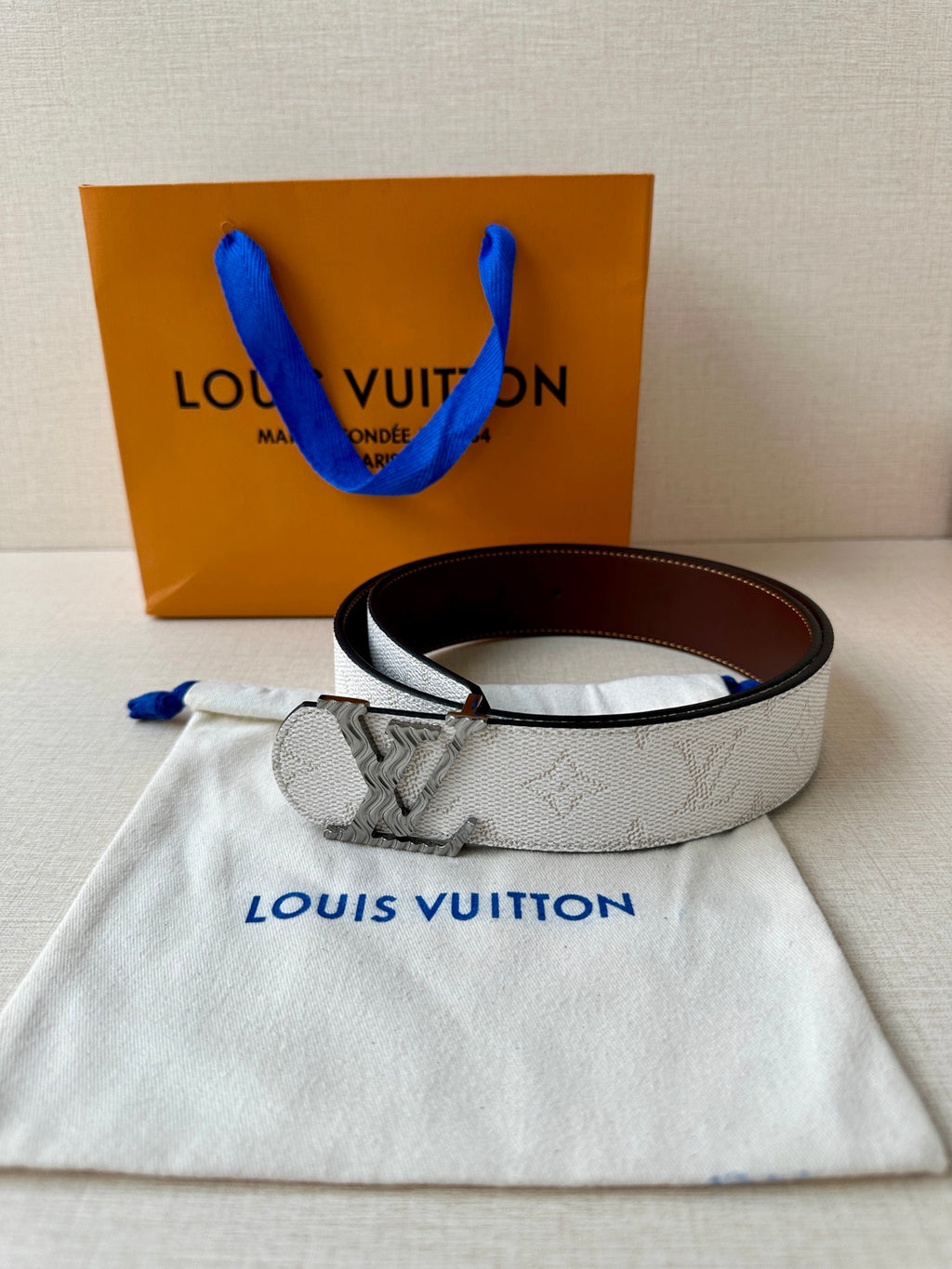 Louis Vuitton belt laid on pouch: light gray textured strap with dark brown buckle