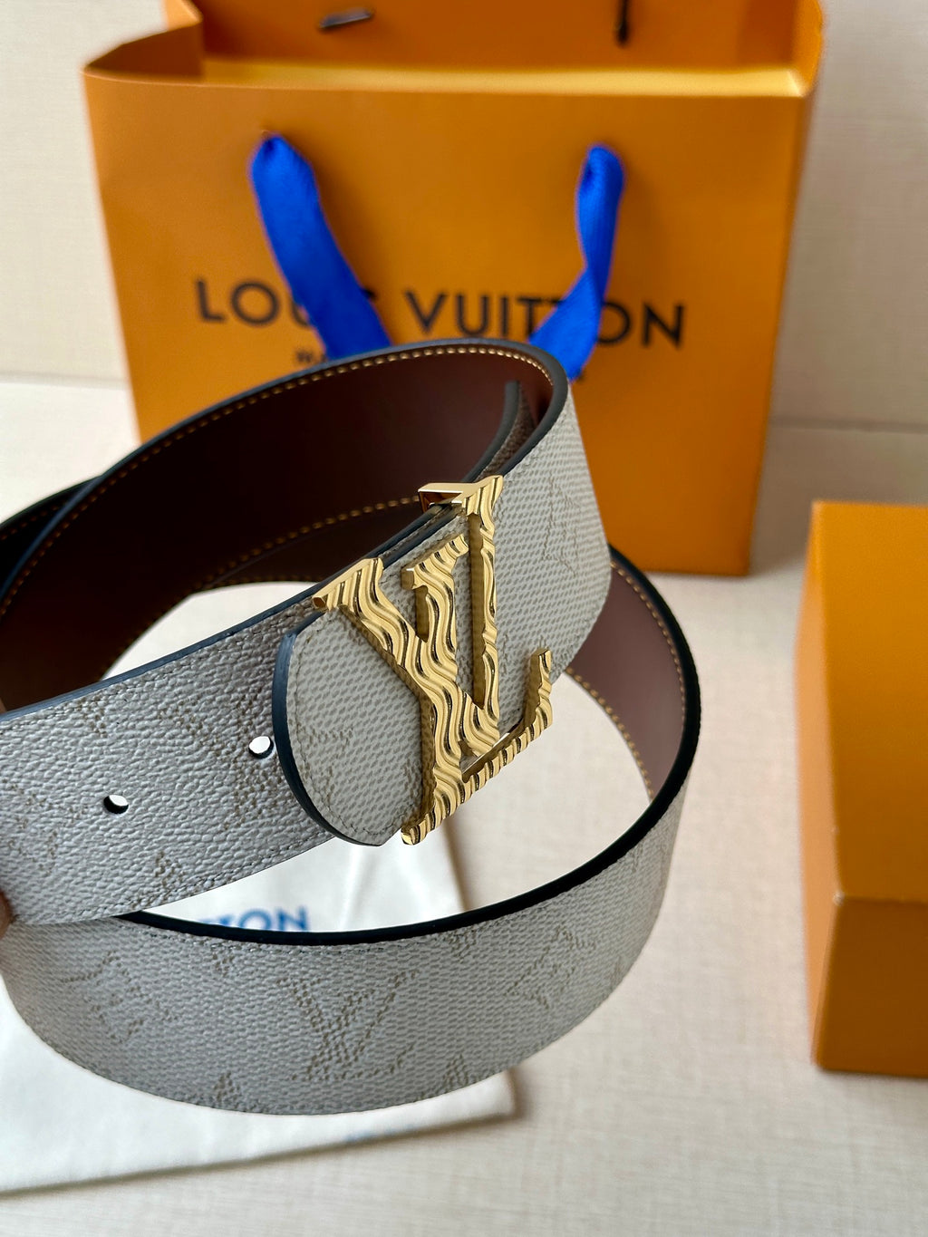 Louis Vuitton belt buckle close-up: light gray textured strap with brown backing