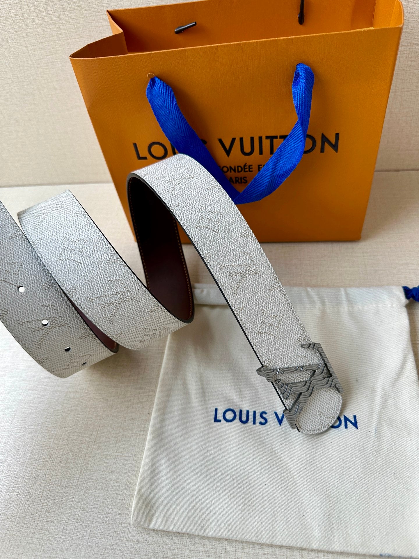 Louis Vuitton belt shown rolled: light gray strap with dark brown inner side