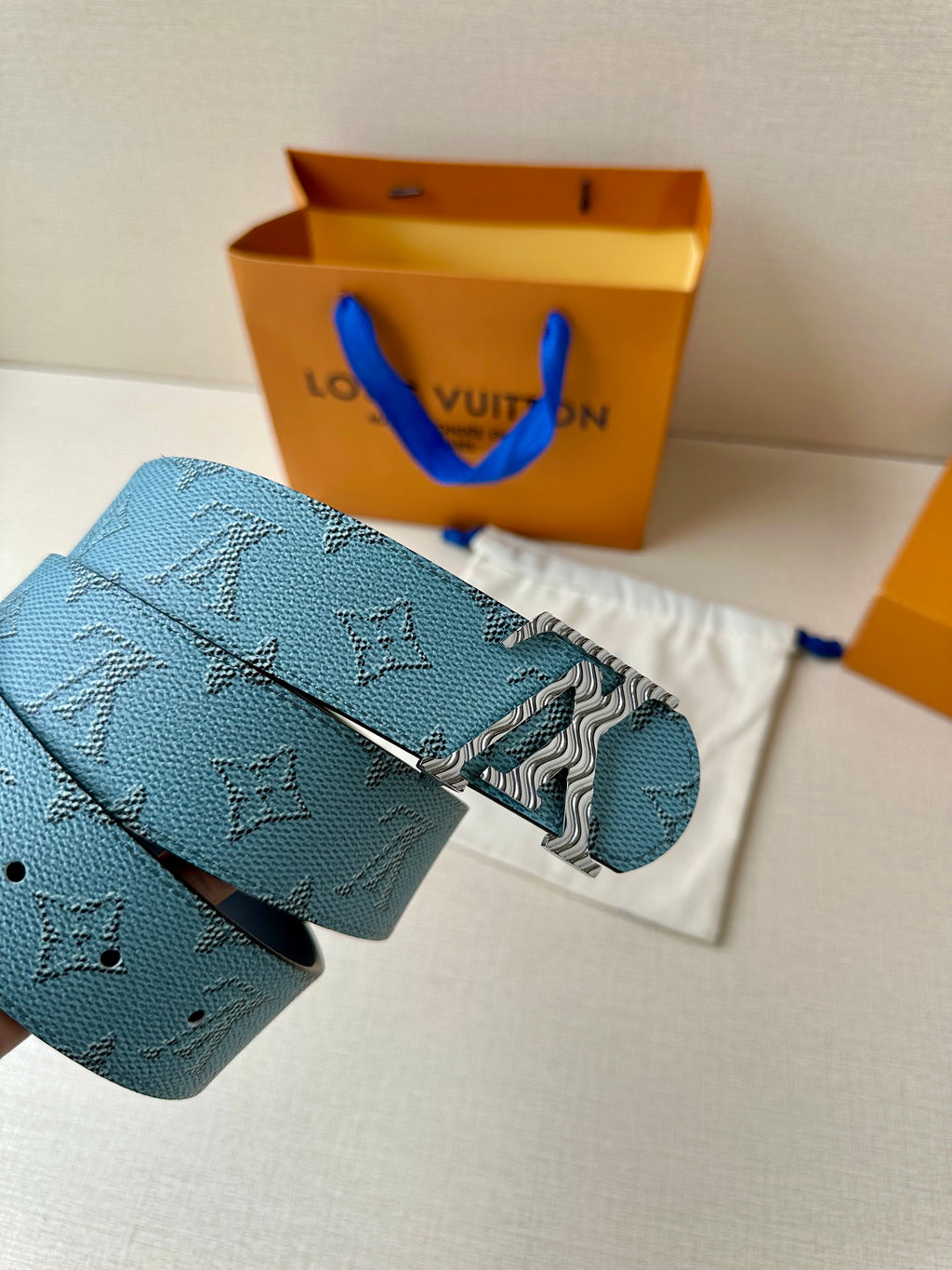Blue monogram belt with gold buckle and black inner strap, close view.