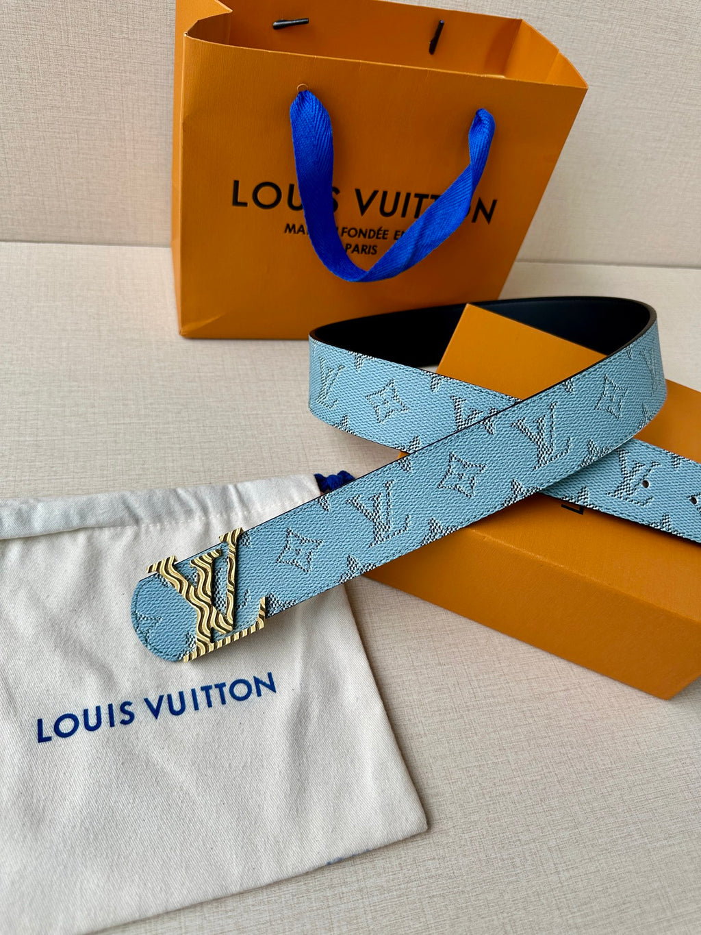 Blue monogram belt with gold buckle, with pouch and orange packaging.