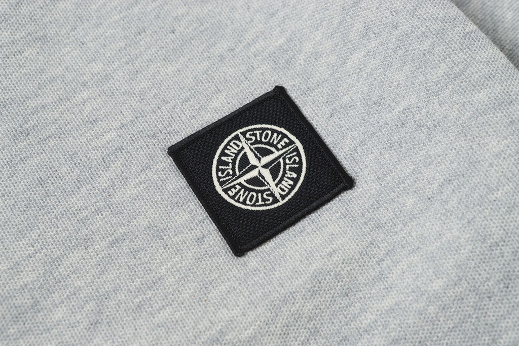 Embroidered black logo patch on light gray polo fabric