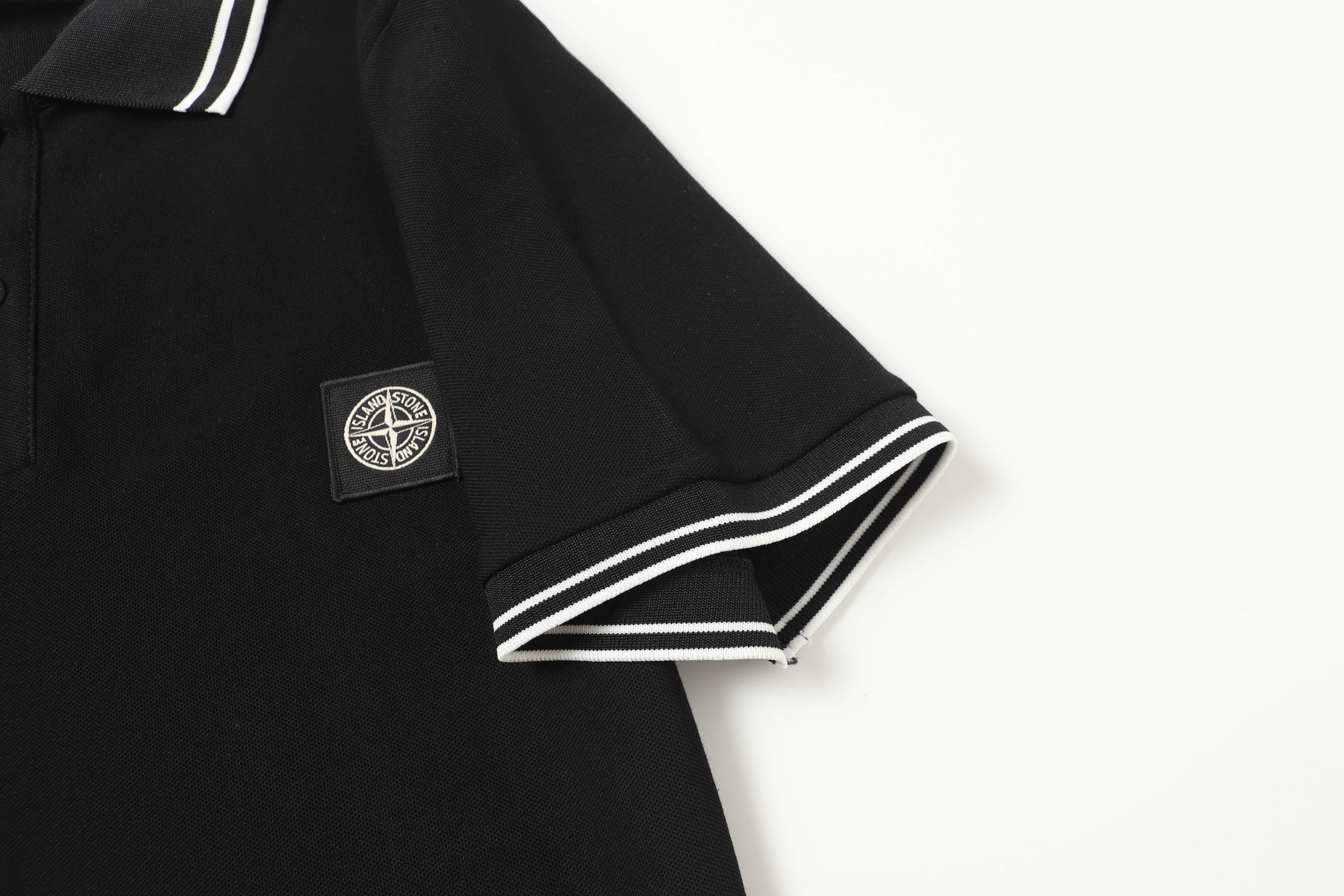 Black polo shirt sleeve with striped cuff and chest logo patch