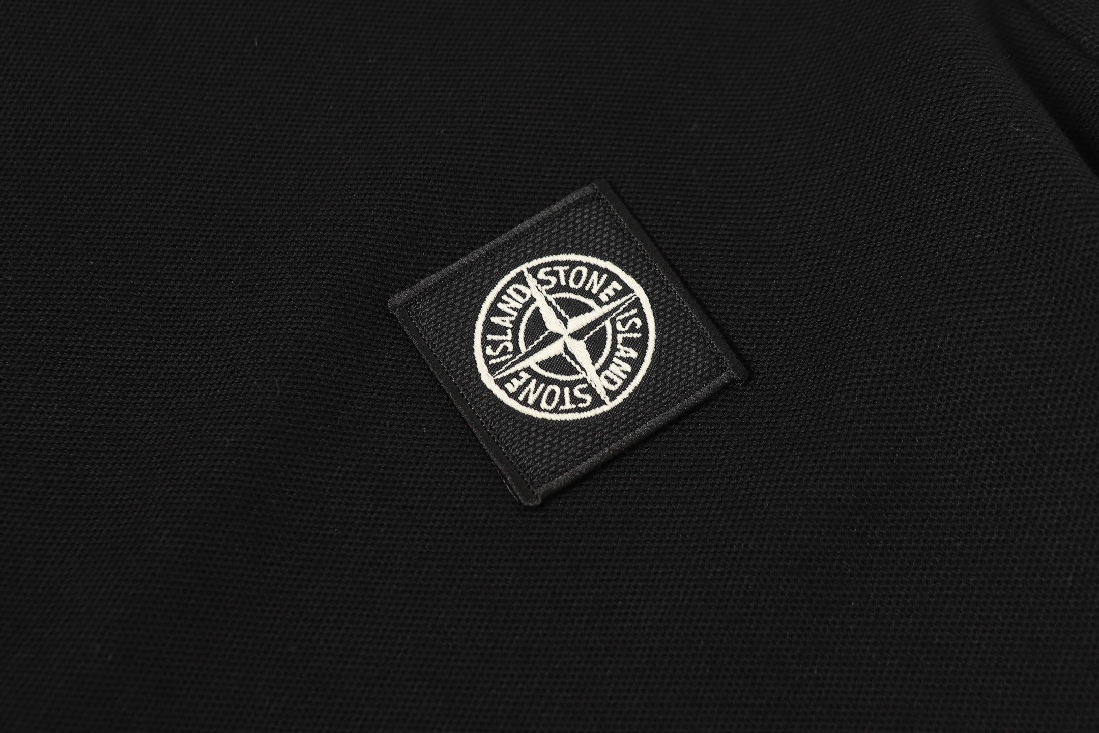 Stone Island circular logo patch on black polo fabric