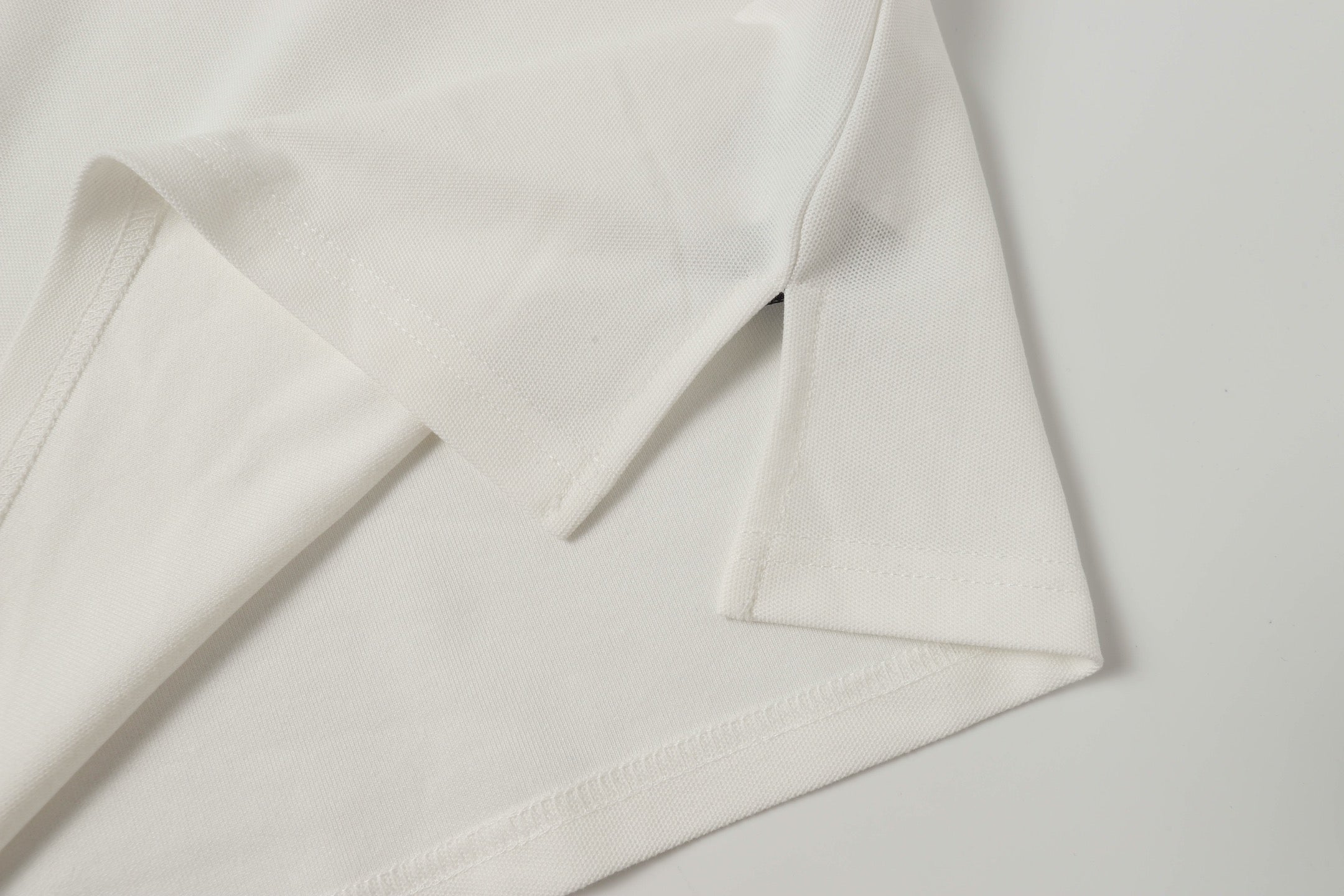 White polo shirt fabric close-up with stitched hem and sleeve