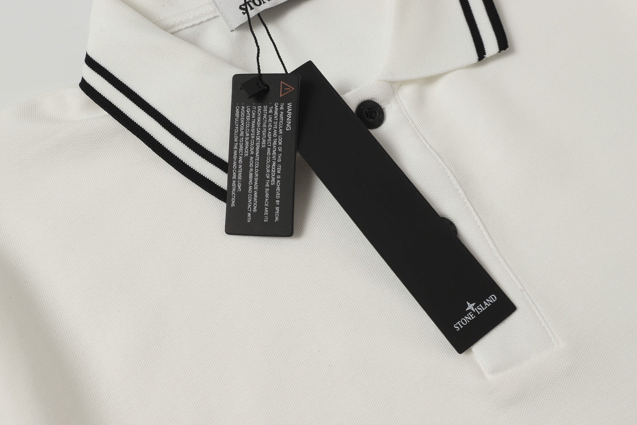 White polo shirt neckline detail with black button and hanging brand tag