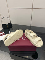 Cream slide sandals on display box; embossed footbed and adjustable strap
