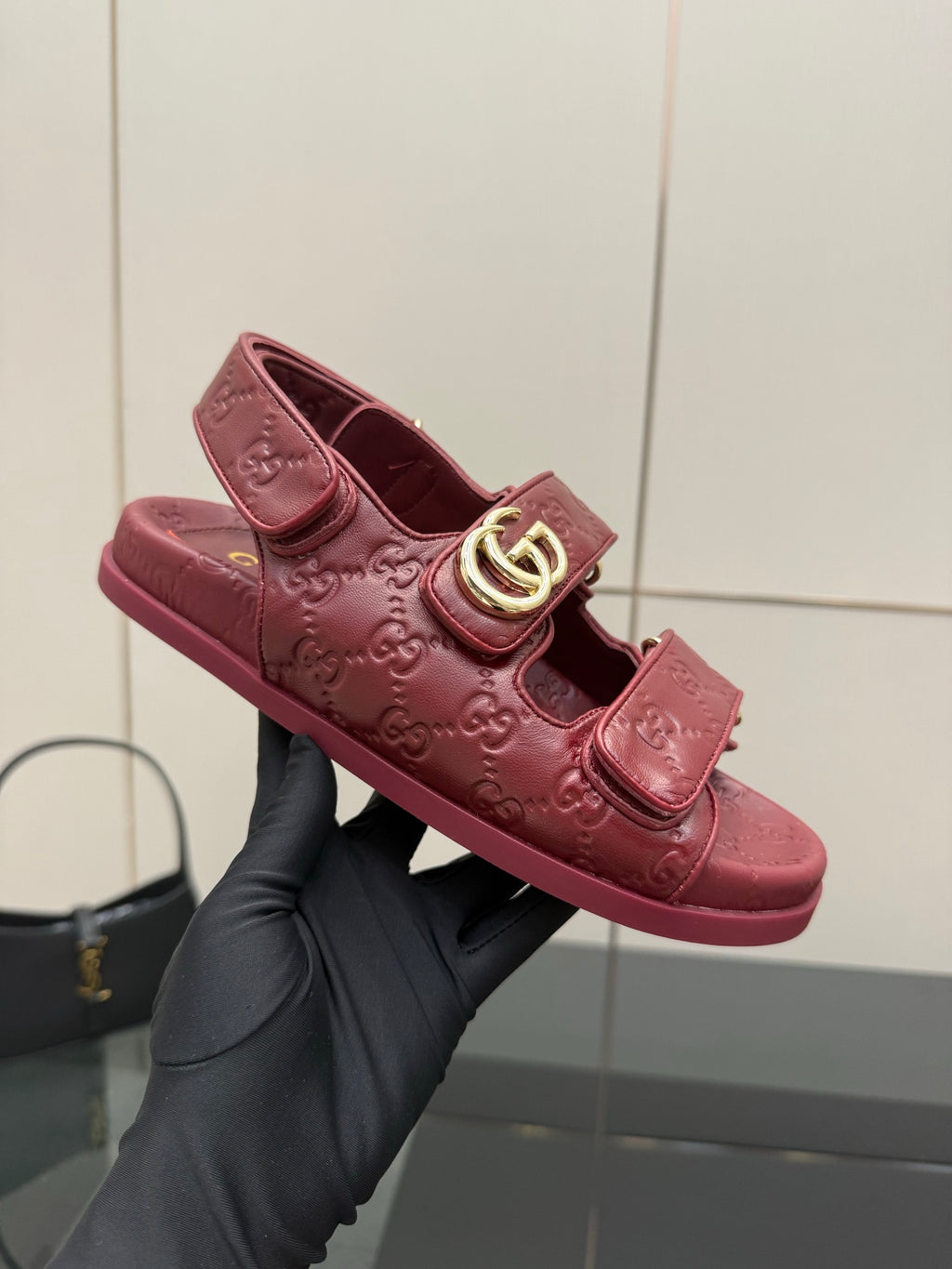 Red Gucci logo-buckle slide sandal held in black glove, top view