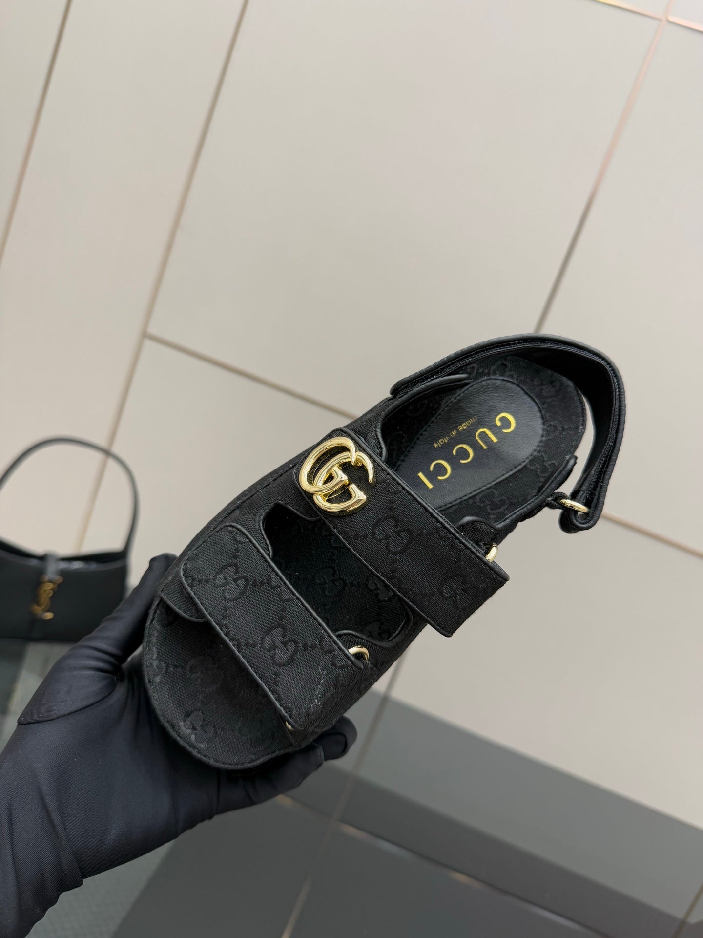 Gucci ladies sandal top view held in hand, dark GG-pattern straps and gold-tone buckle