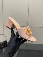 Gucci women’s mule slides in light pink with gold buckle, held by hand in glove
