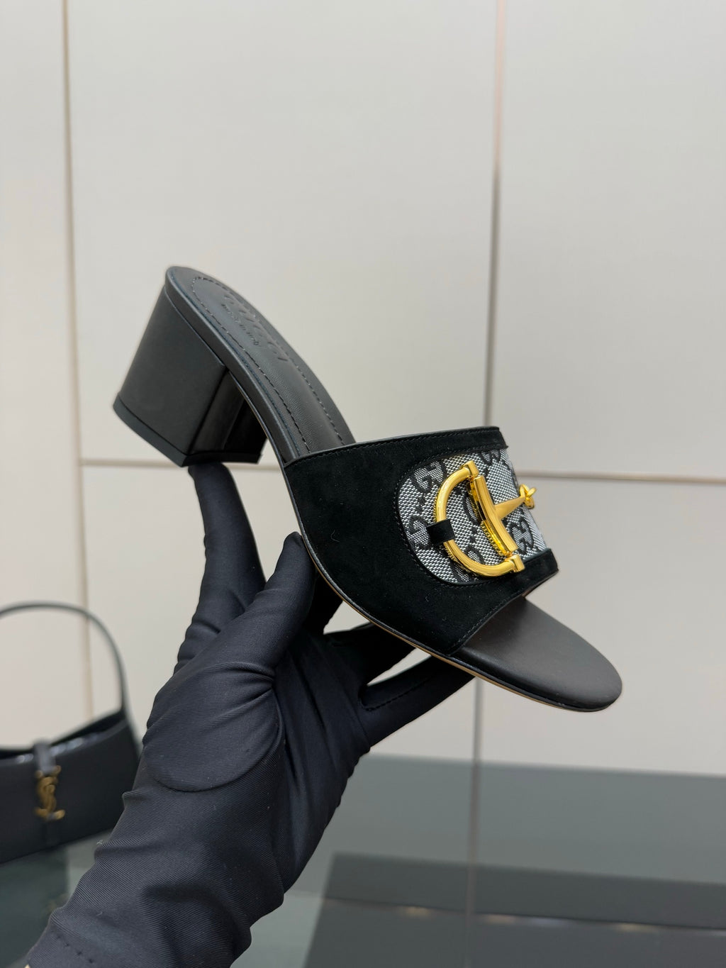 Black slide sandal with GG-print strap and gold buckle, side view in hand