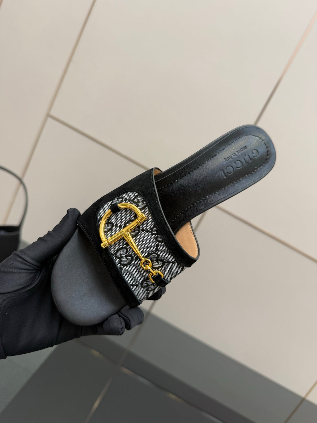 Black slide sandal with GG-print strap and gold buckle, held side view