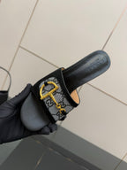 Black slide sandal with GG-print strap and gold buckle, held side view