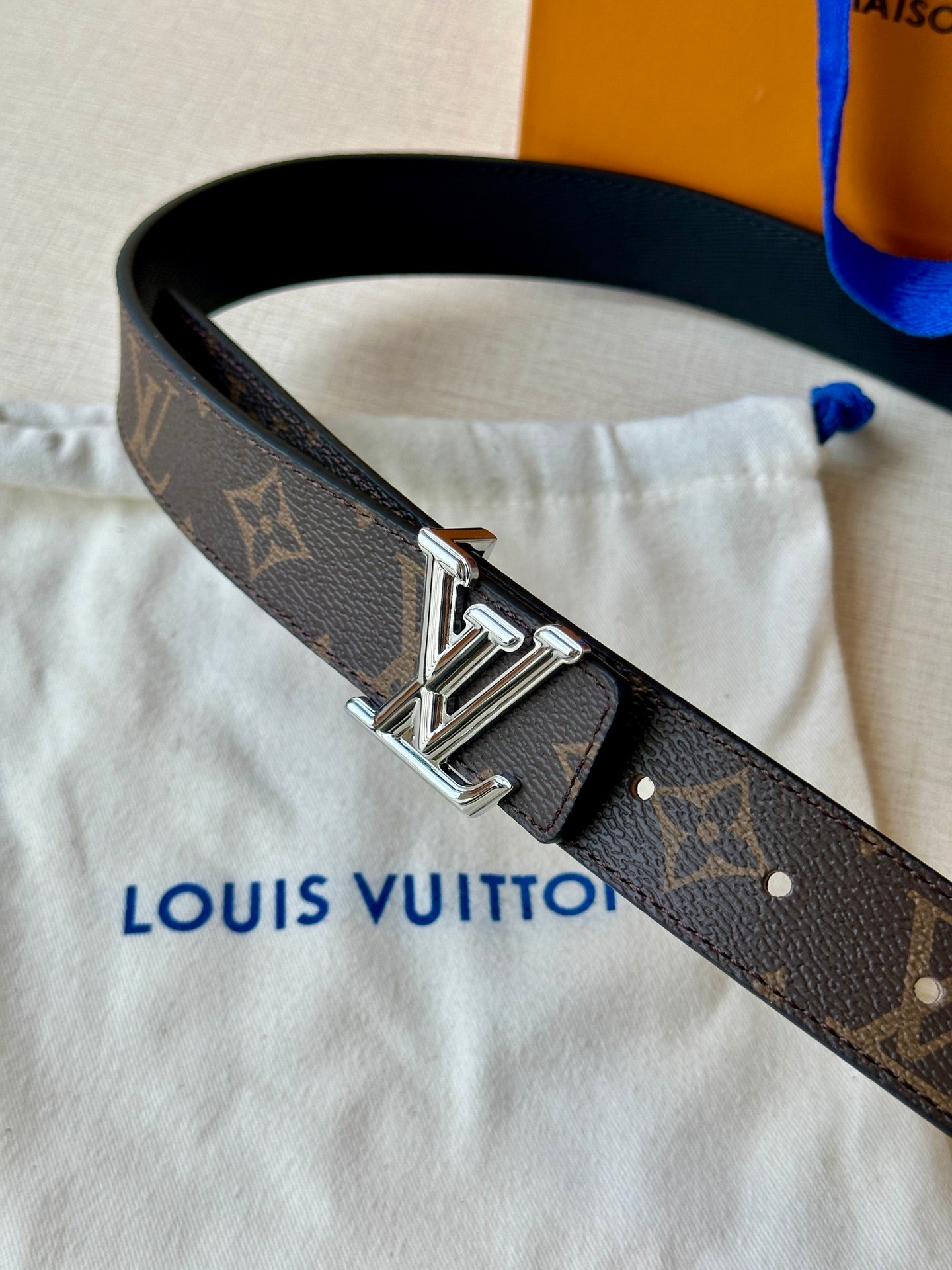Brown monogram leather belt close-up with polished metal buckle and stitched end