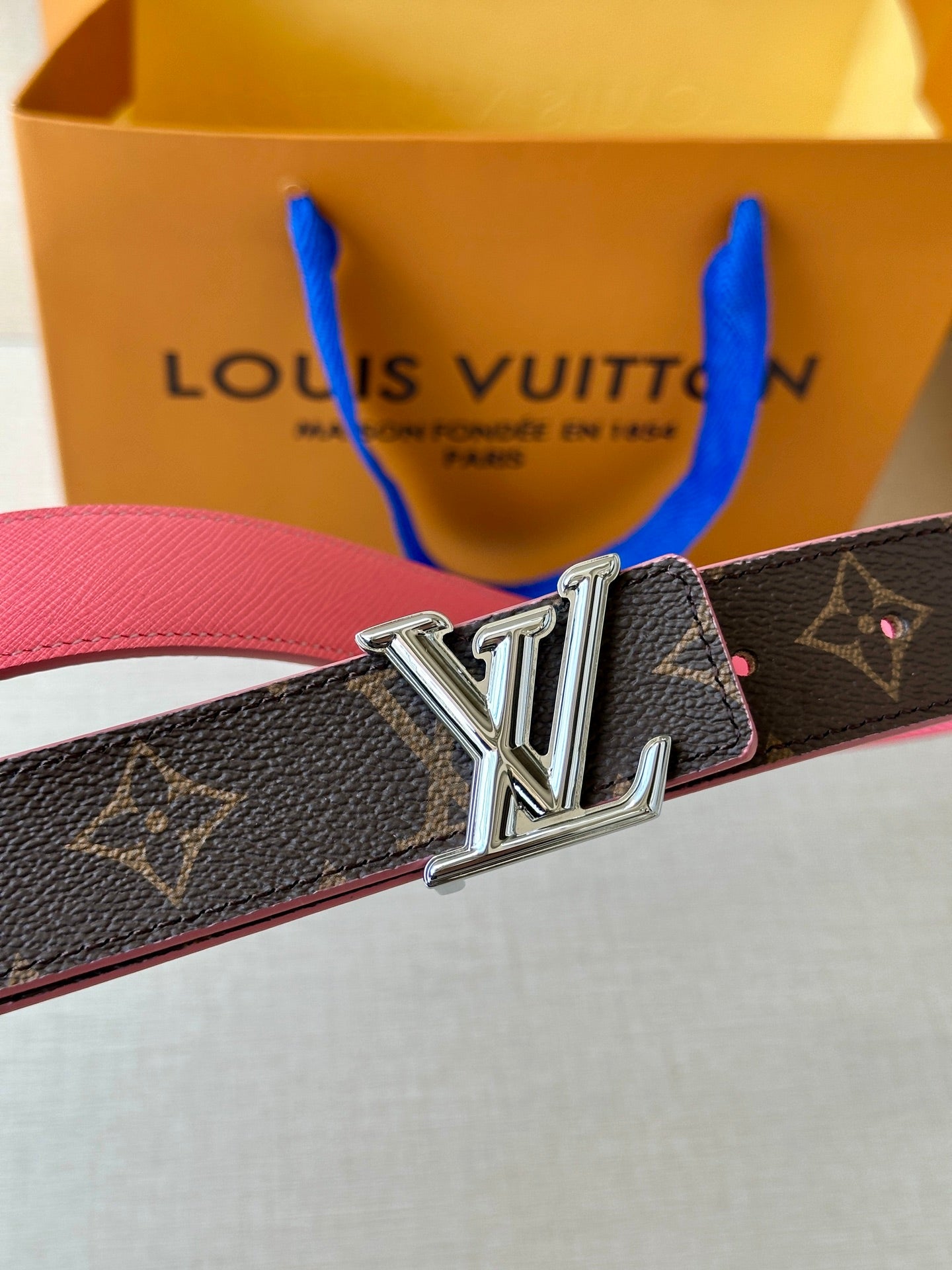 Belt buckle detail: dark monogram canvas strap with silver LV buckle and pink edge