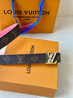 Dark monogram belt with silver LV buckle across orange box, pink trim visible