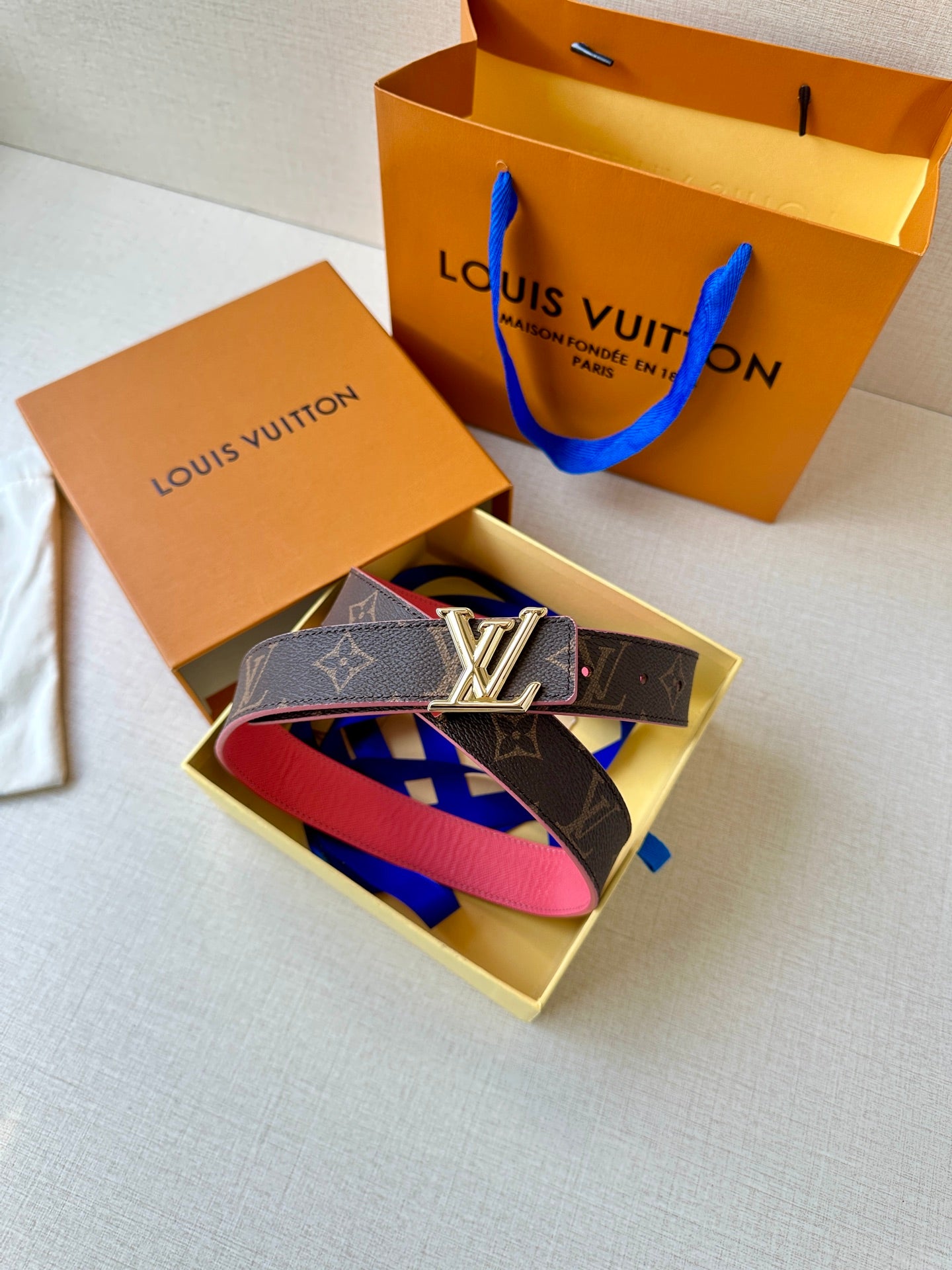 Dark monogram belt with silver LV buckle and pink strap, styled in gift box