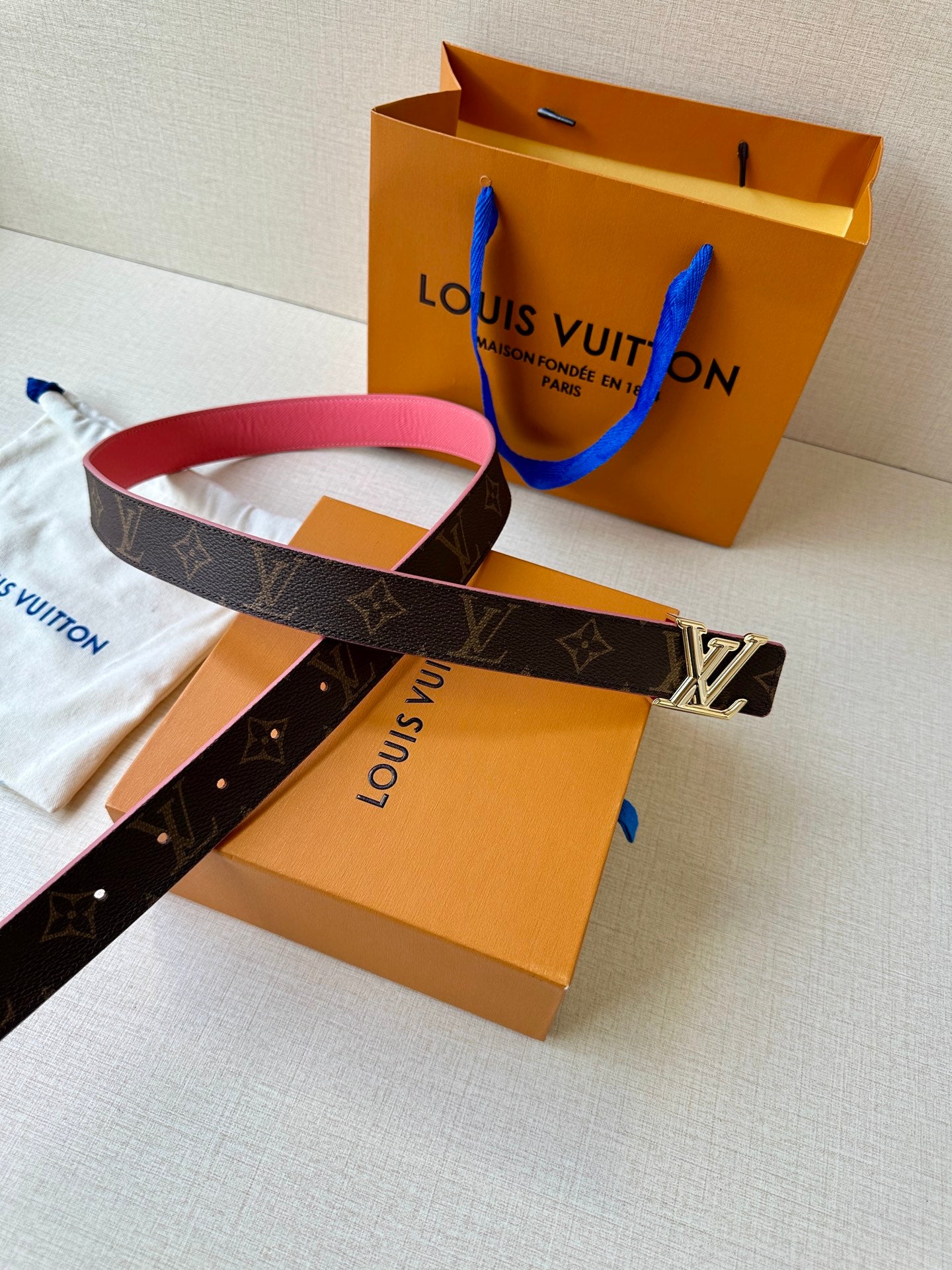 Monogram belt with silver LV buckle and pink strap on orange boxes and pouch