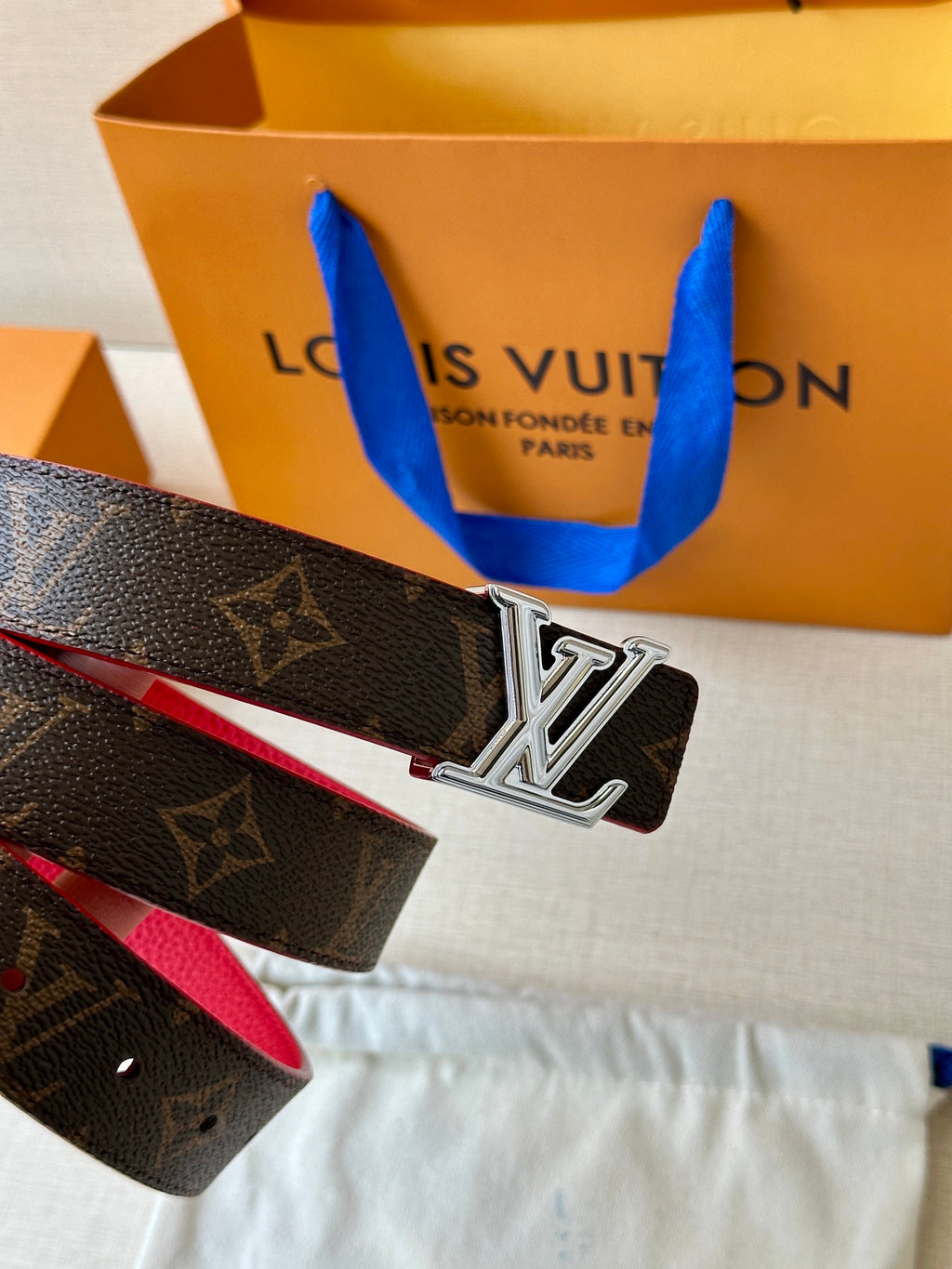 Louis Vuitton monogram belt with silver LV buckle and red interior, angled