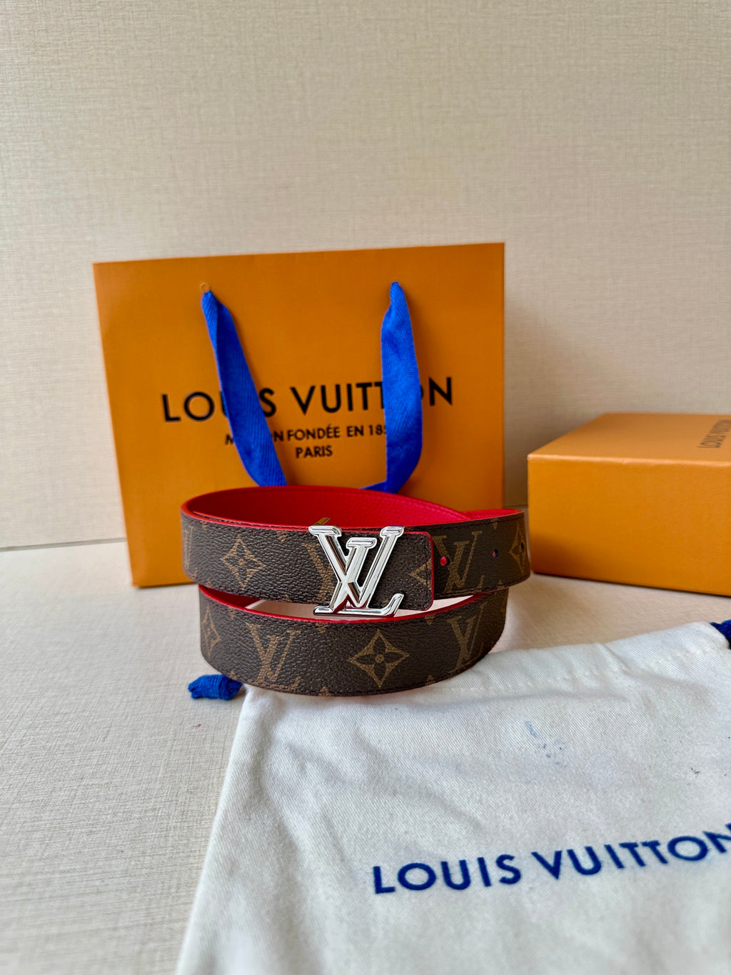Louis Vuitton monogram belt with red underside and silver LV buckle on dust bag