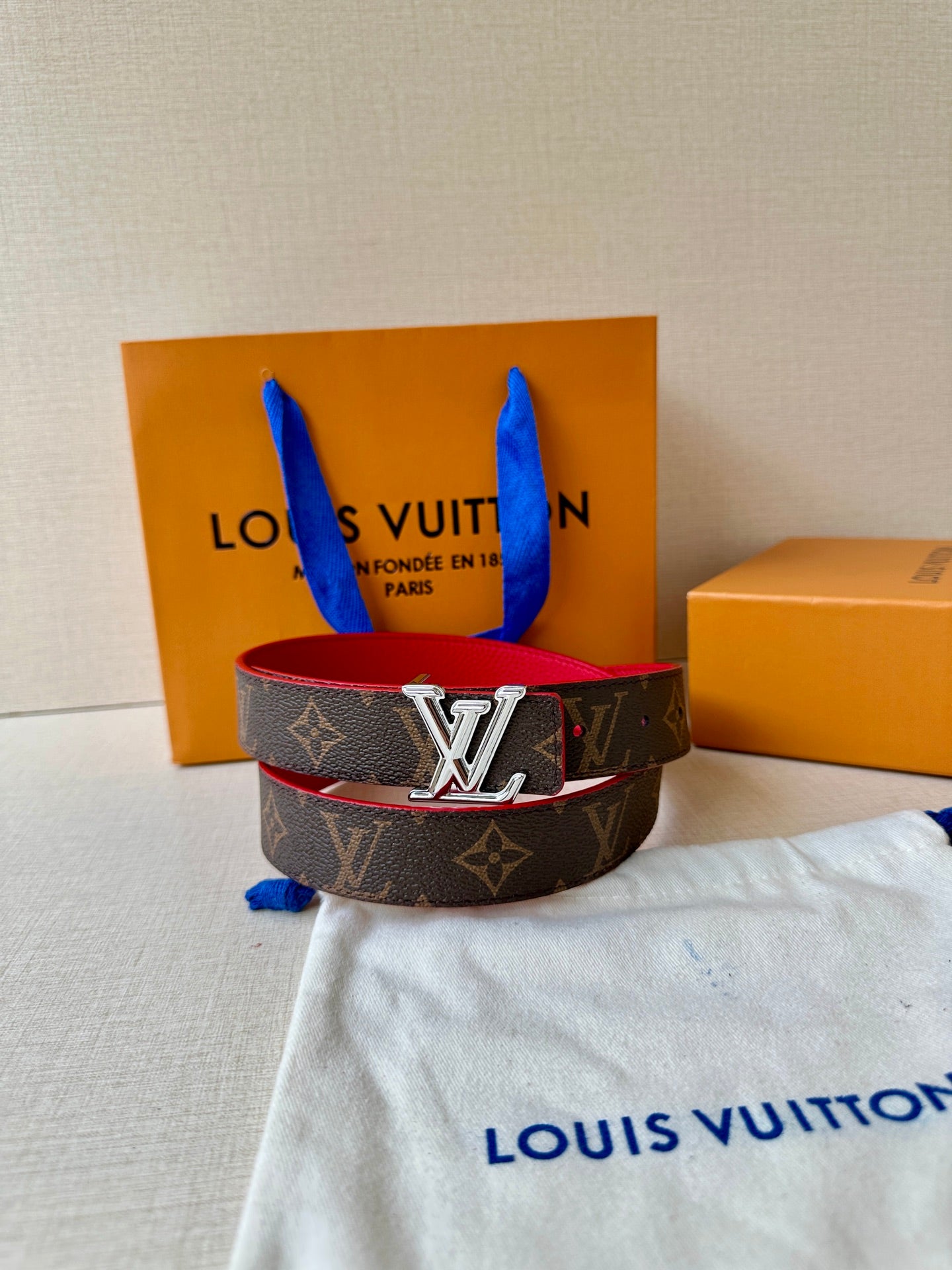 Louis Vuitton monogram belt with red underside and silver LV buckle on dust bag