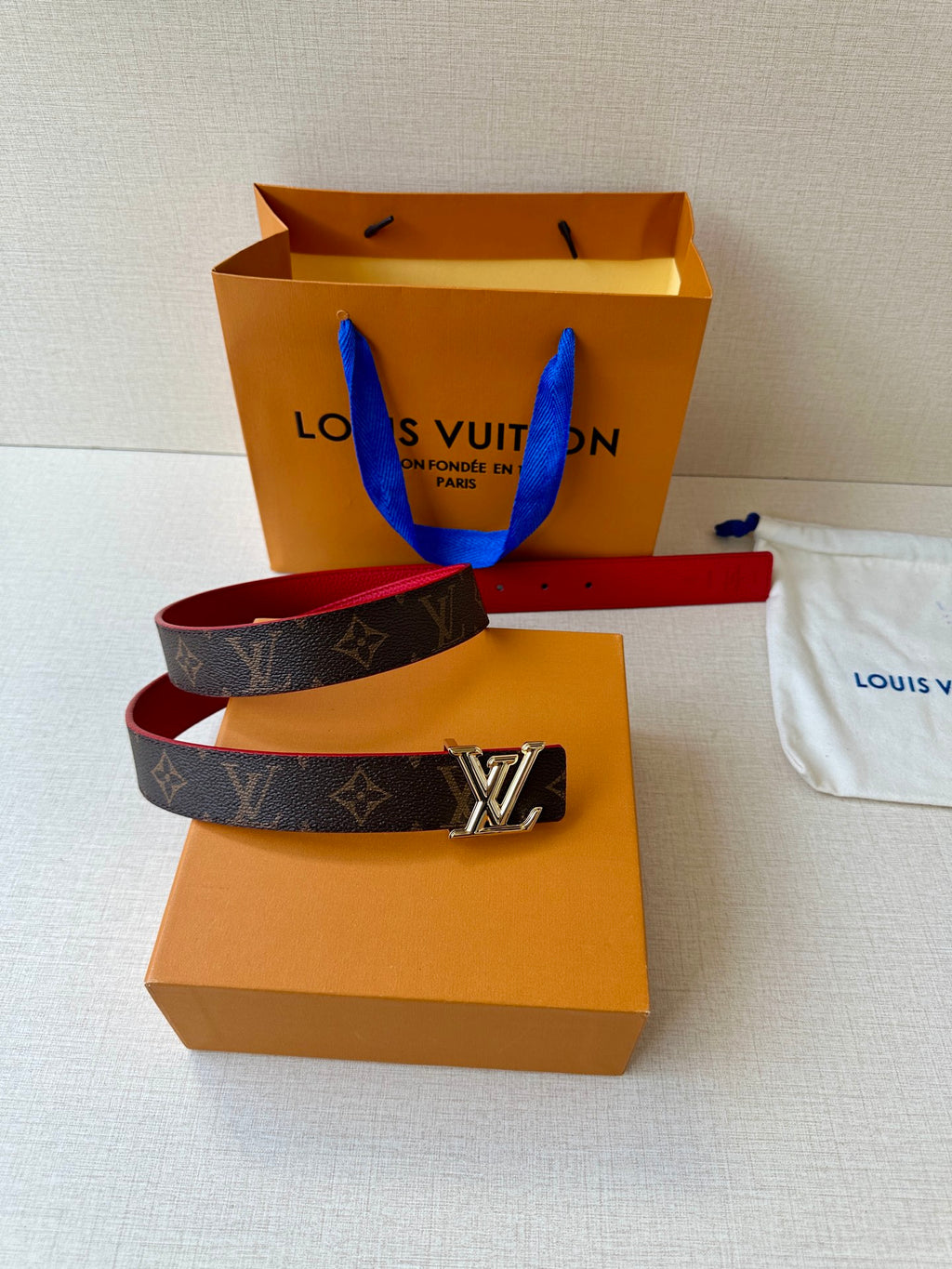 Louis Vuitton monogram belt with red interior and silver LV buckle on dust bag