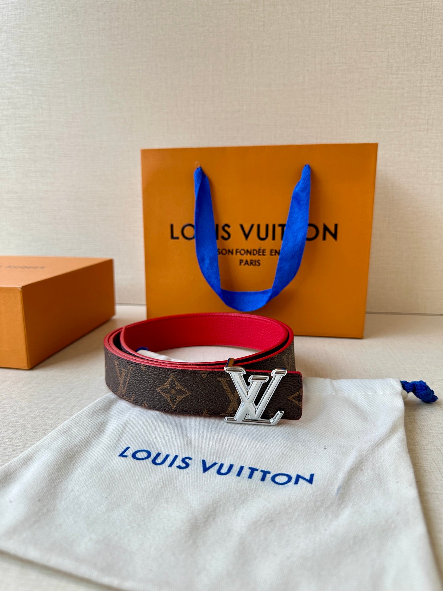 Louis Vuitton monogram belt with red interior and silver LV buckle, coiled