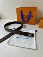 Brown monogram leather belt with gold-tone buckle on white dust bag near orange bag