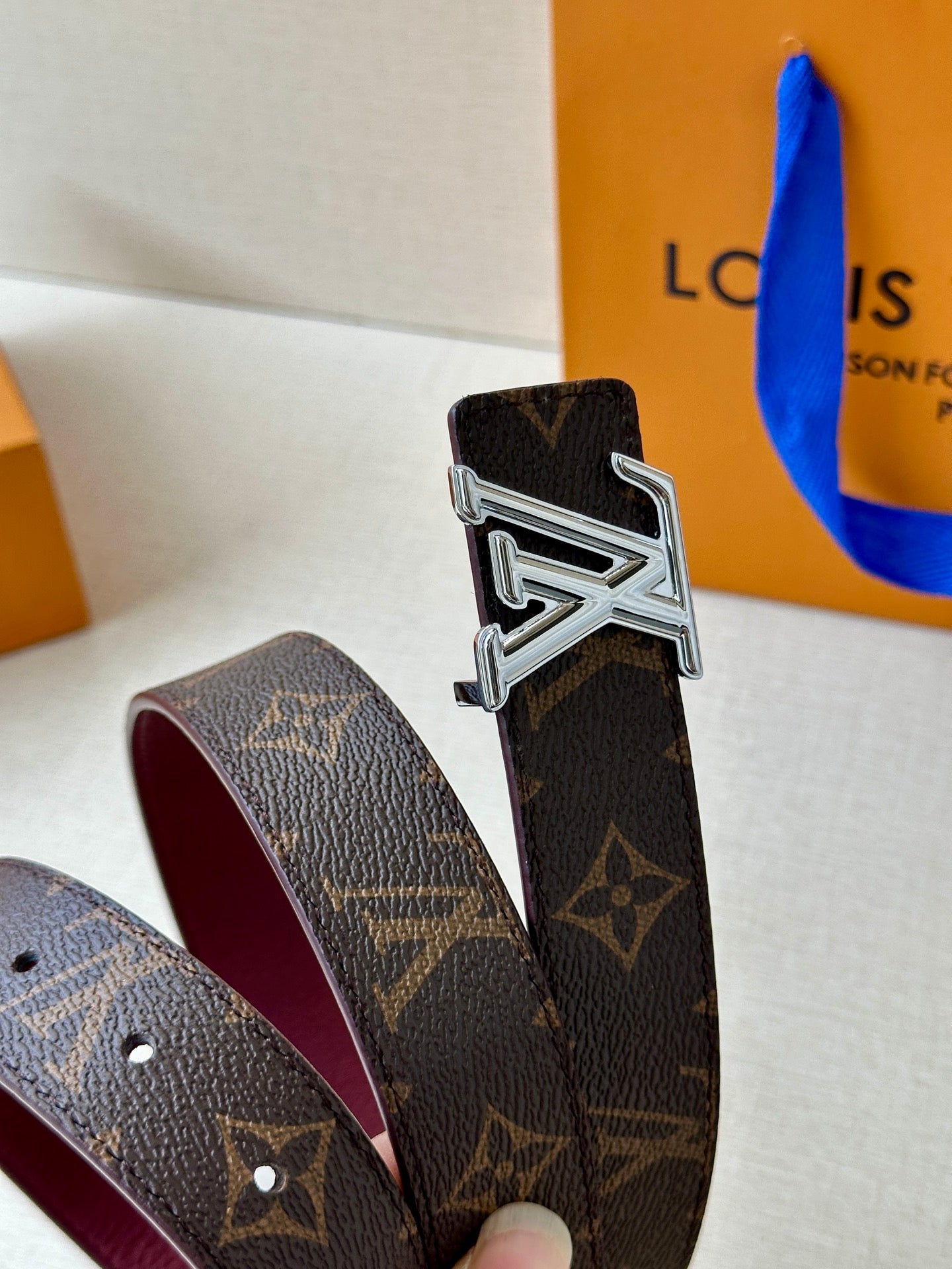 Louis Vuitton monogram belt close-up with silver buckle and burgundy underside