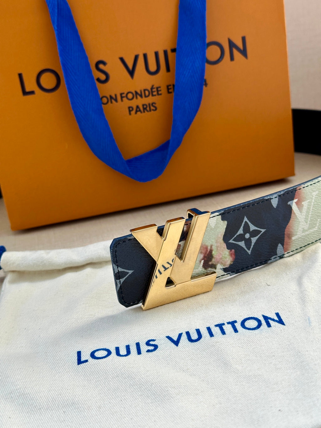 Monogram leather belt with gold-tone LV buckle on multicolor patterned strap.