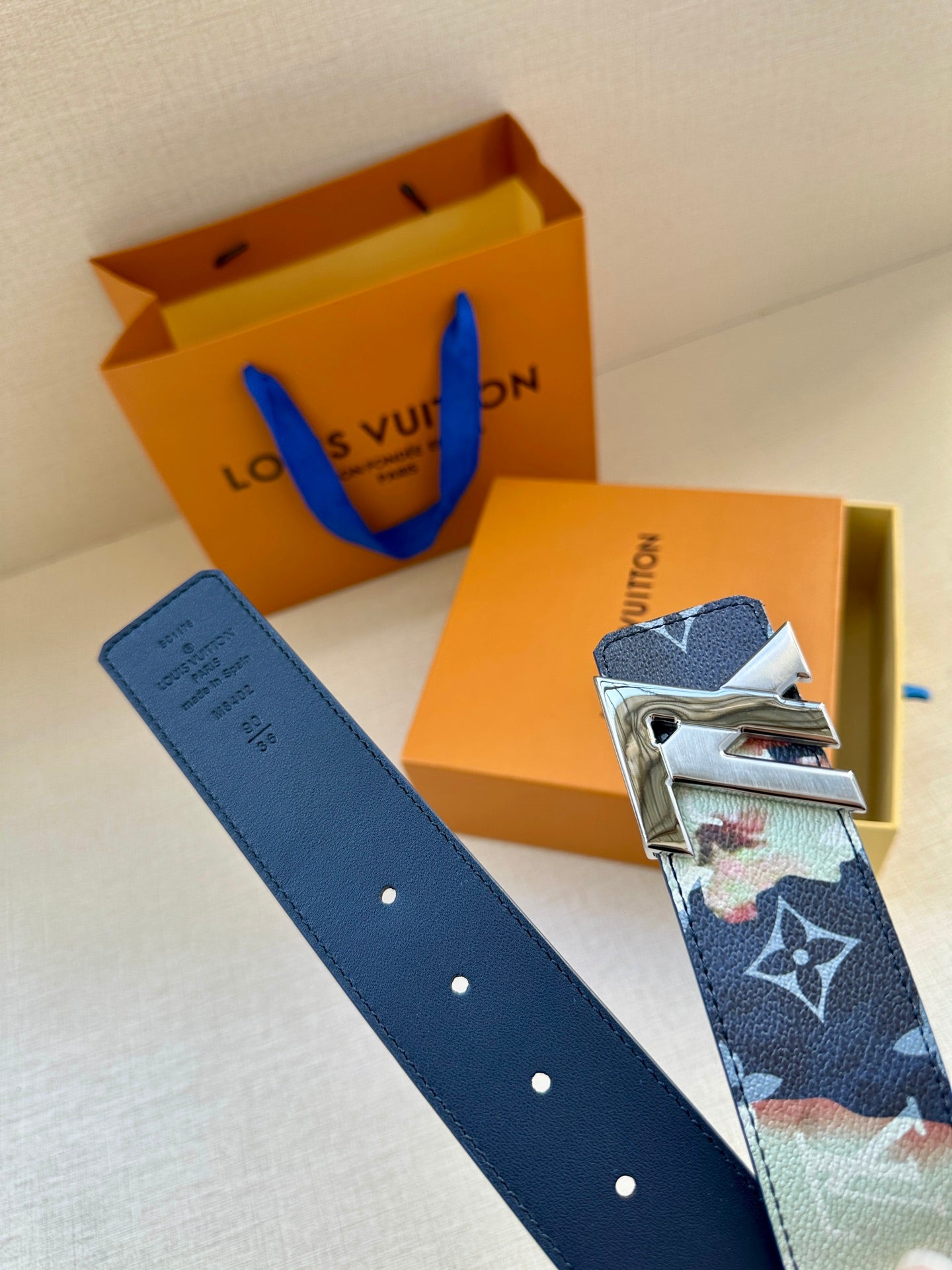 Two-tone monogram leather belt with gold-tone LV buckle and navy eyelets.