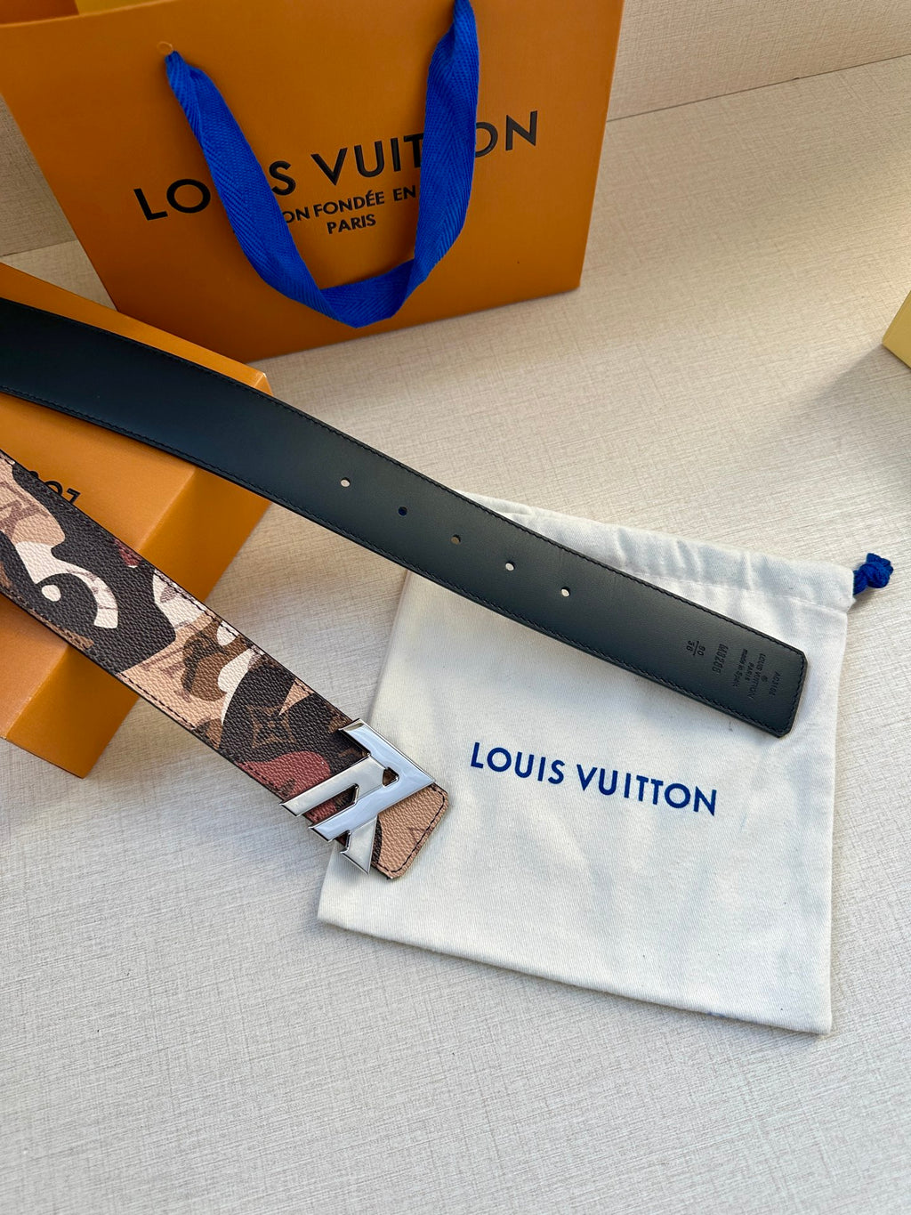 Monogram belt with gold-tone buckle and black leather strap on dust bag