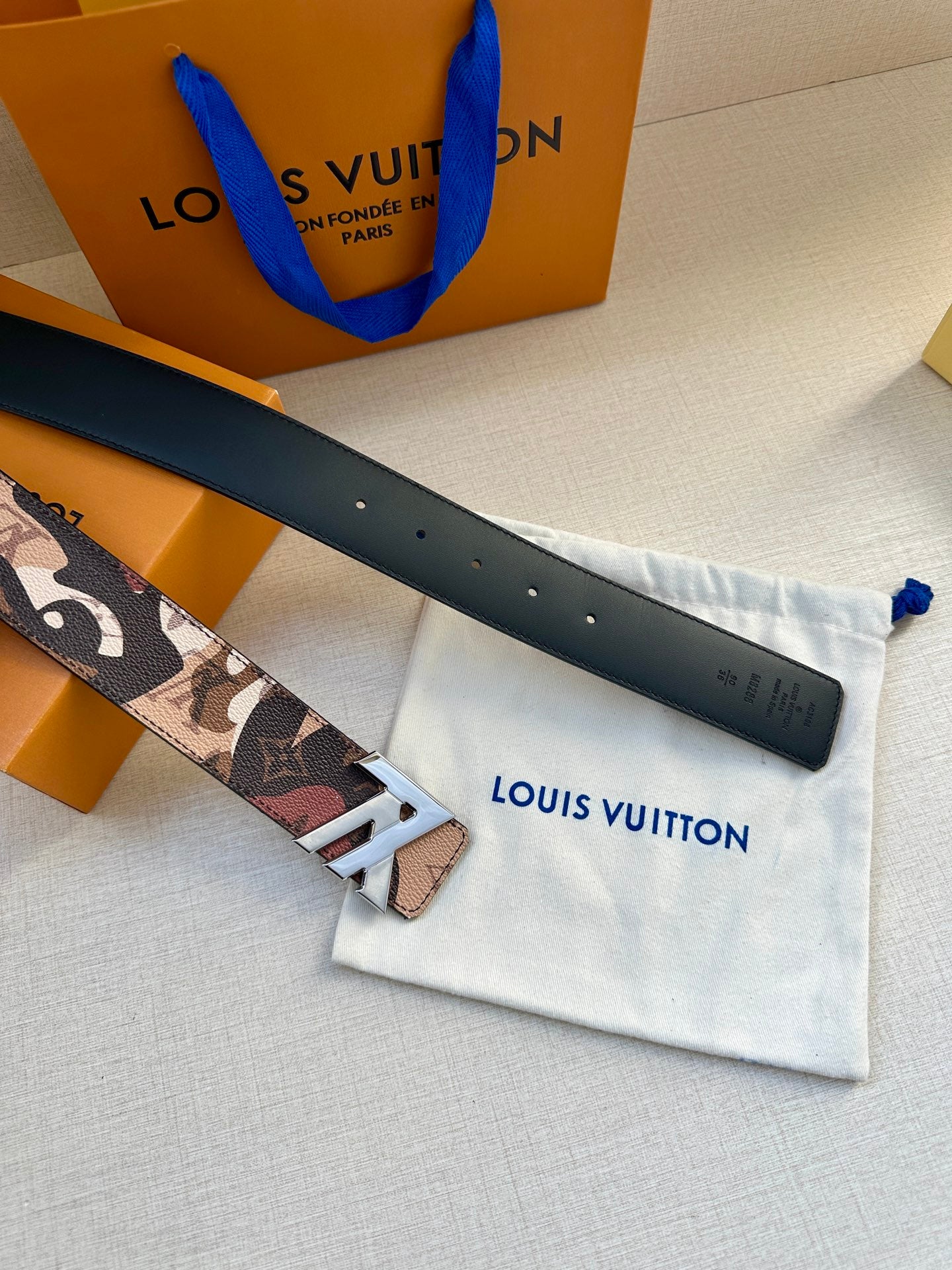 Monogram belt with gold-tone buckle and black leather strap on dust bag