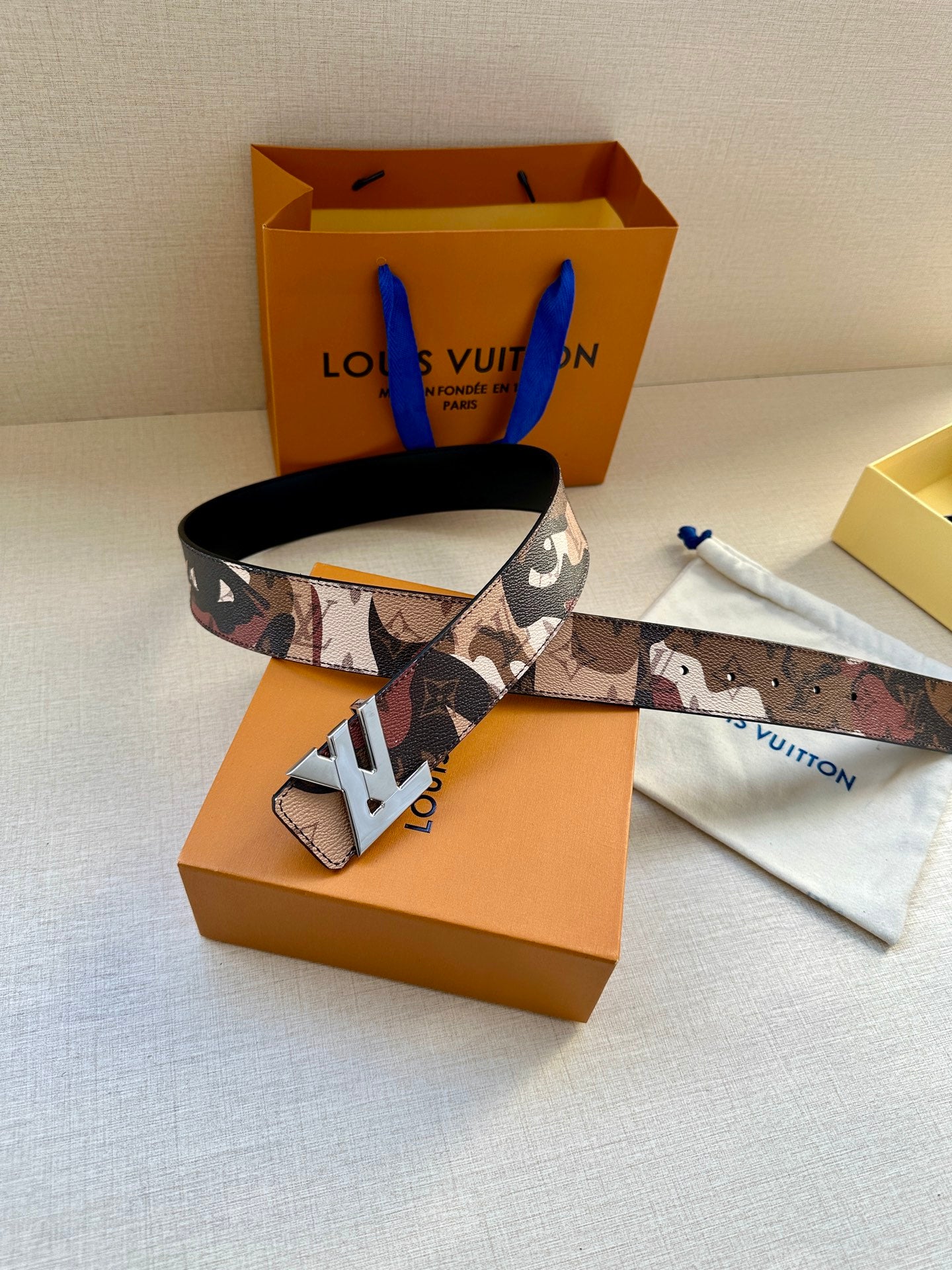 Monogram belt with gold-tone buckle, laid across packaging and dust bag