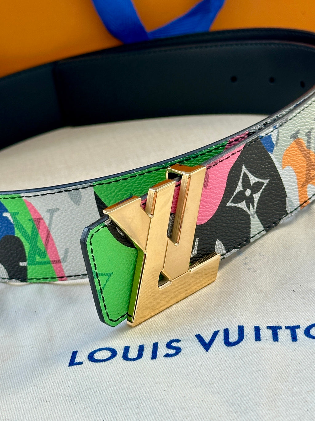 Belt close-up: multicolor graphic strap with gold buckle and green leather insert