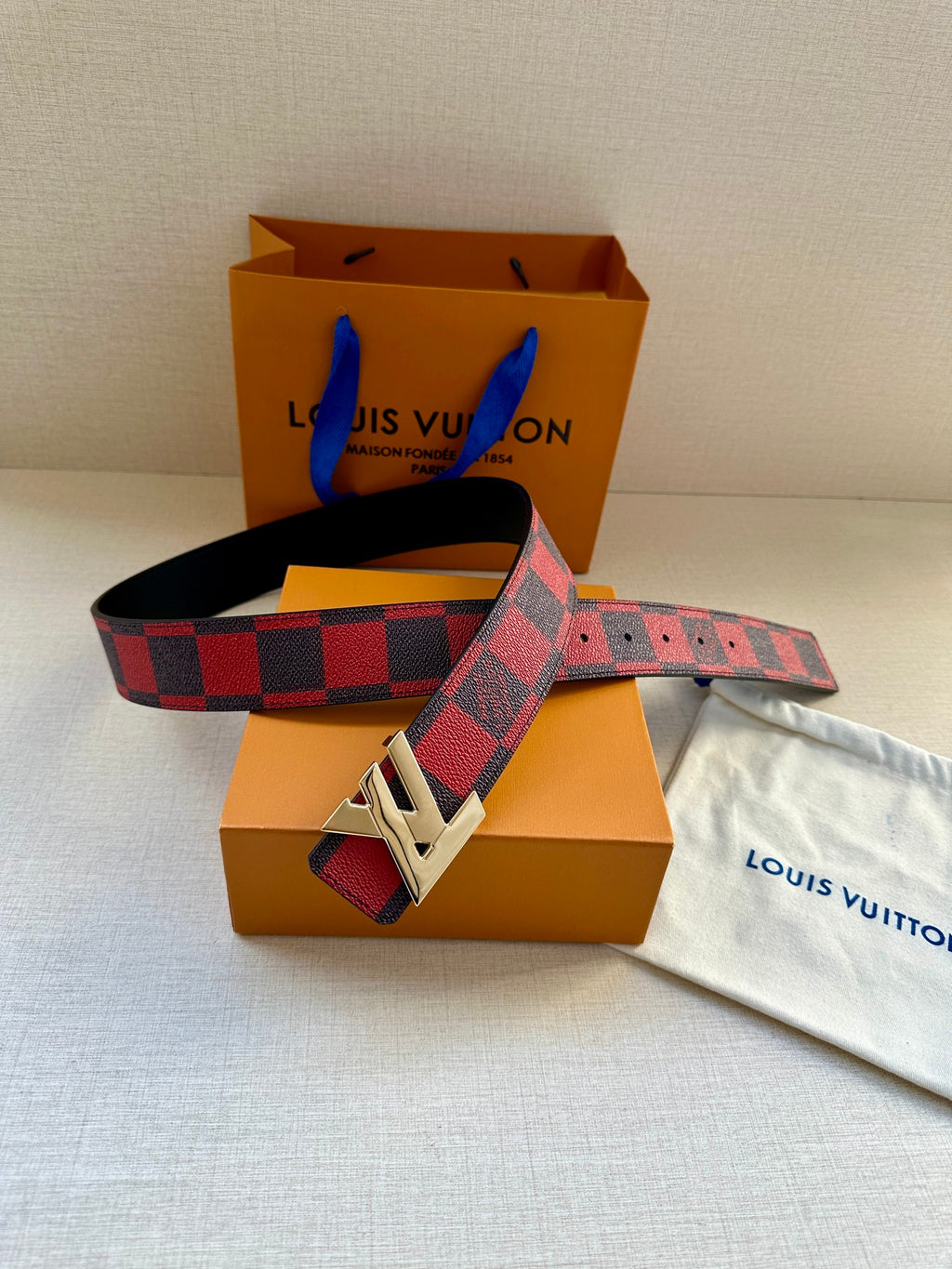Louis Vuitton belt with checkered strap and gold buckle, across retail packaging