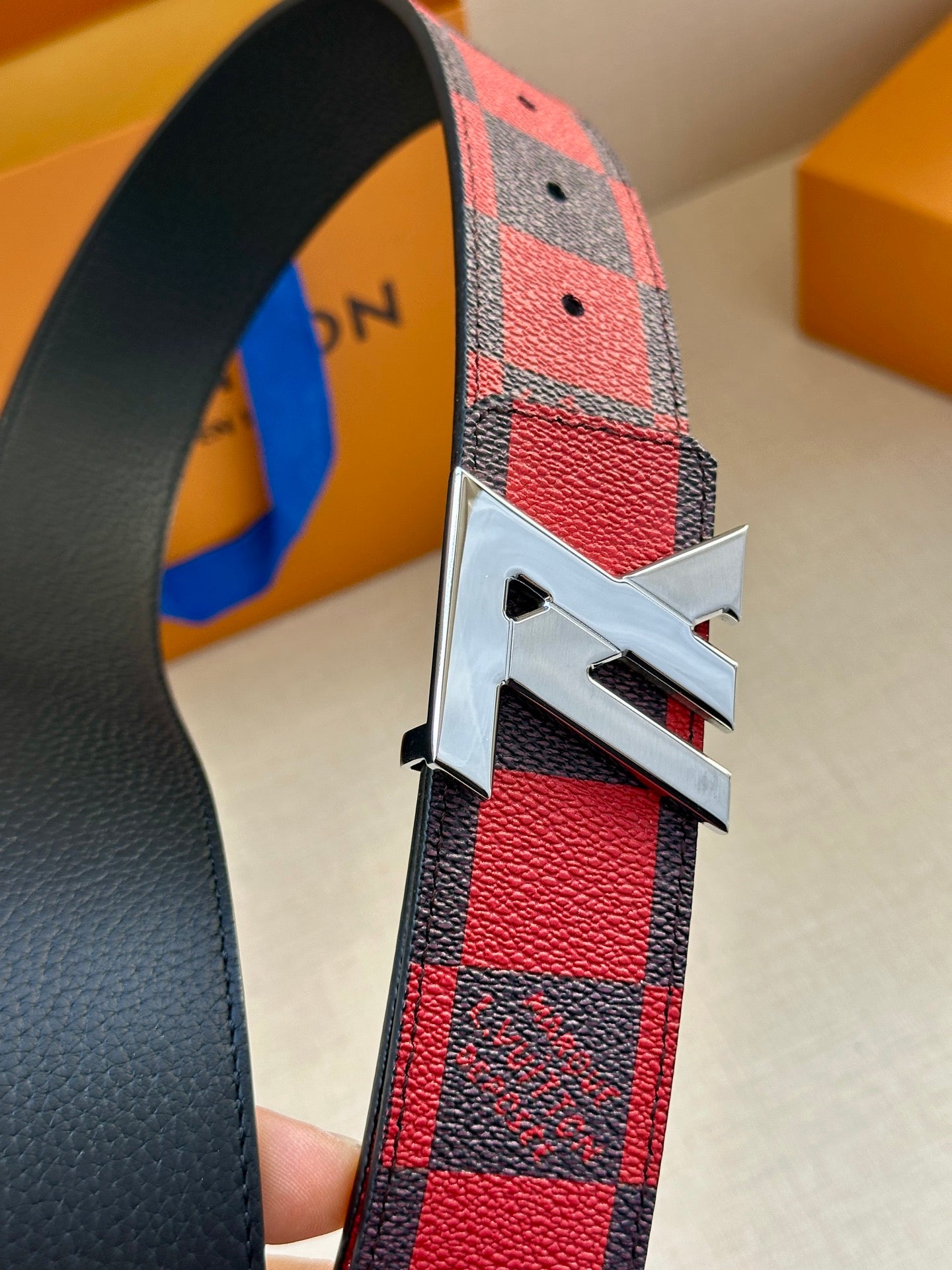 Louis Vuitton belt close-up with red and black check strap and gold LV buckle