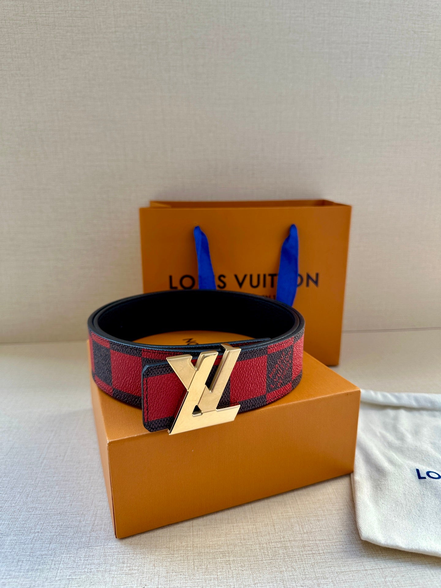 Louis Vuitton belt with red and black check strap and gold LV buckle, upright