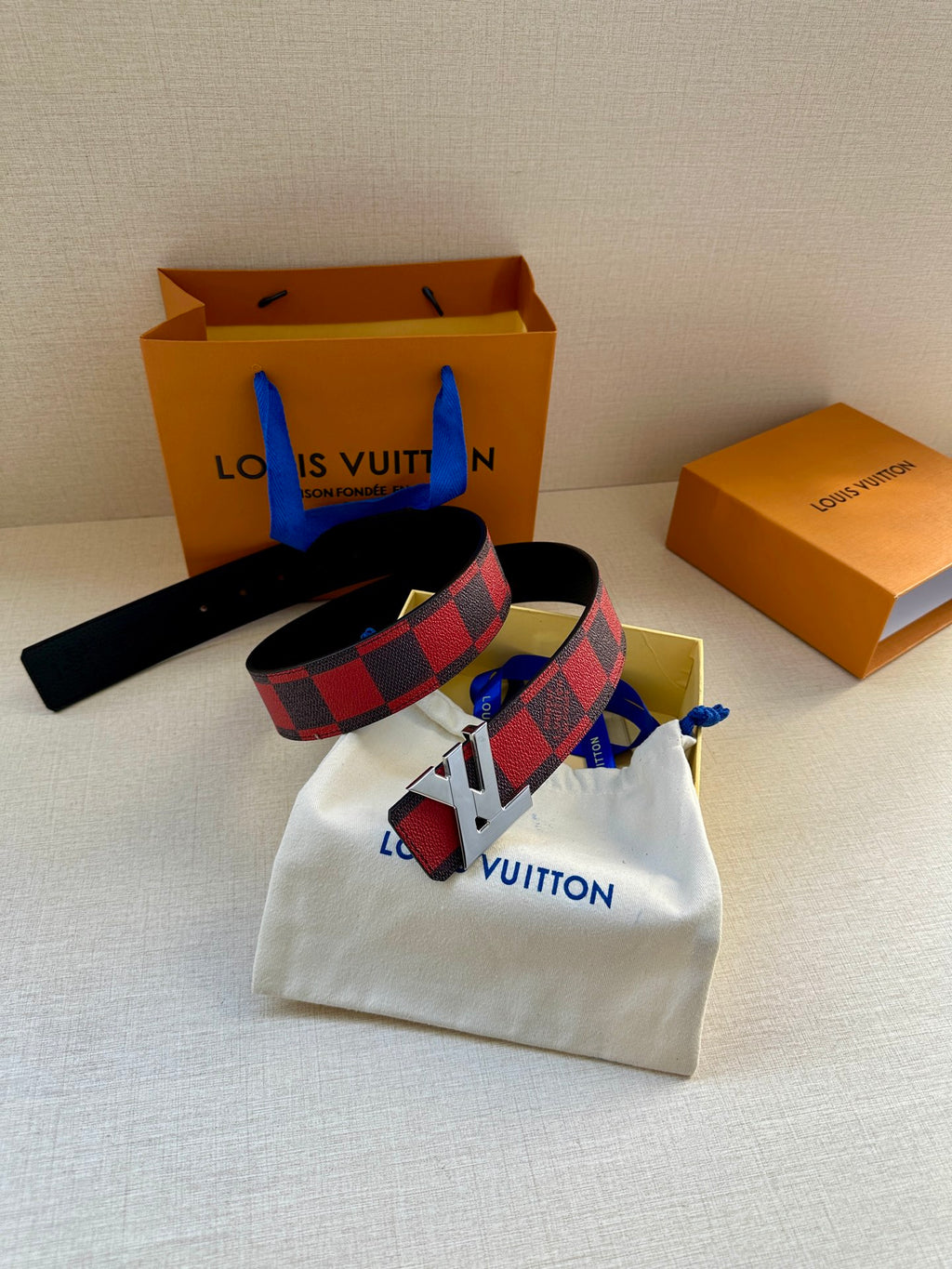 Louis Vuitton belt with checkered strap and gold buckle, laid on white pouch