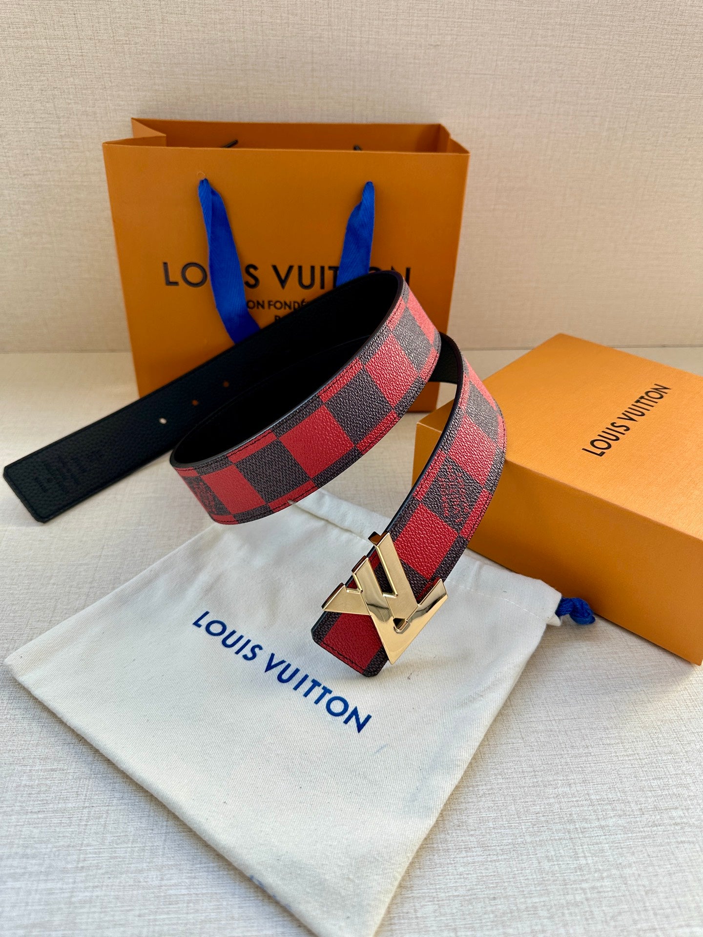 Louis Vuitton belt with checkered strap and gold buckle, resting on white pouch