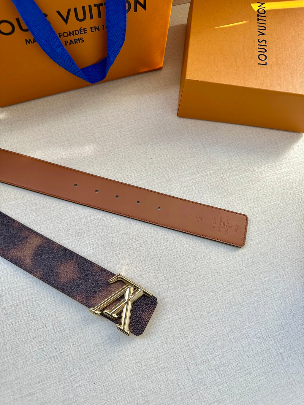 Dark brown leather belt with gold-tone LV buckle and row of punched holes.
